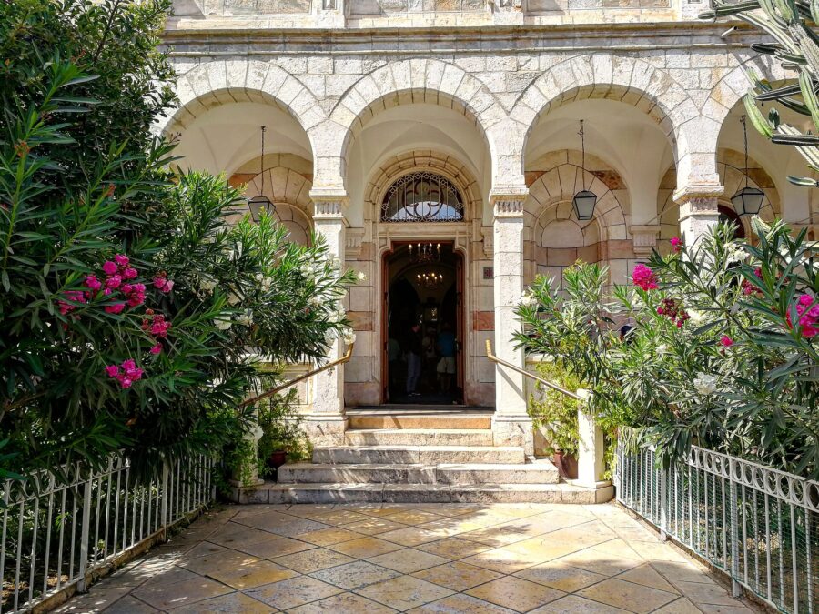 Arcaded stone entrance of the Austrian Hospice in Jerusalem's Old City, with steps up to an open door framed by pink and white oleanders and hanging lanterns