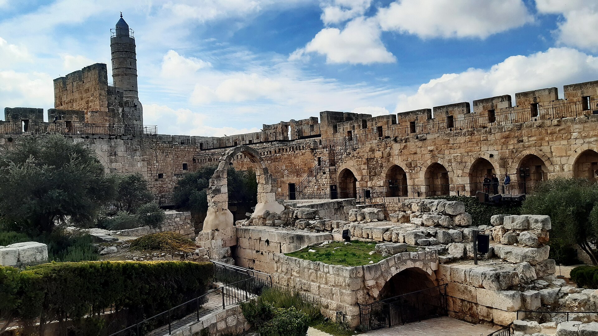 The archaeological garden inside the Tower of David citadel, with excavated walls and a lone stone arch below arcaded ramparts and the minaret tower