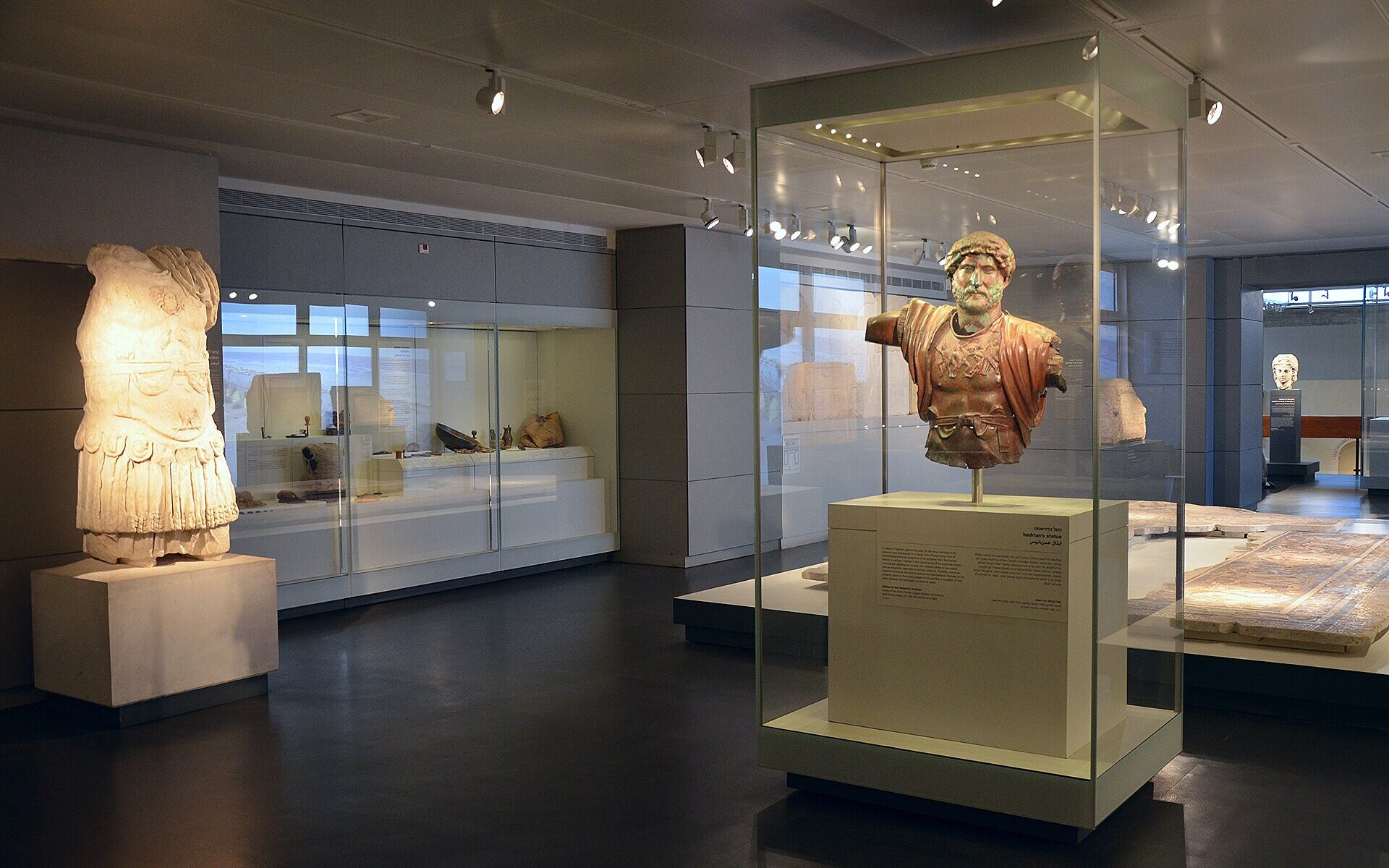 Archaeology gallery at the Israel Museum, with a bronze bust of the emperor Hadrian in a glass case, a headless marble statue in armour and lit display cases