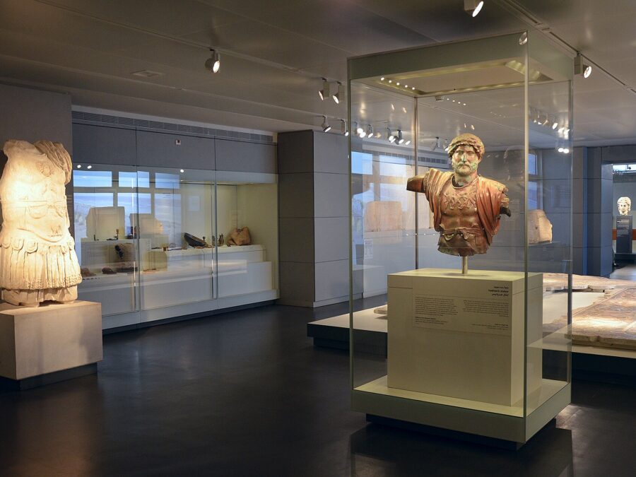 Archaeology gallery at the Israel Museum, with a bronze bust of the emperor Hadrian in a glass case, a headless marble statue in armour and lit display cases
