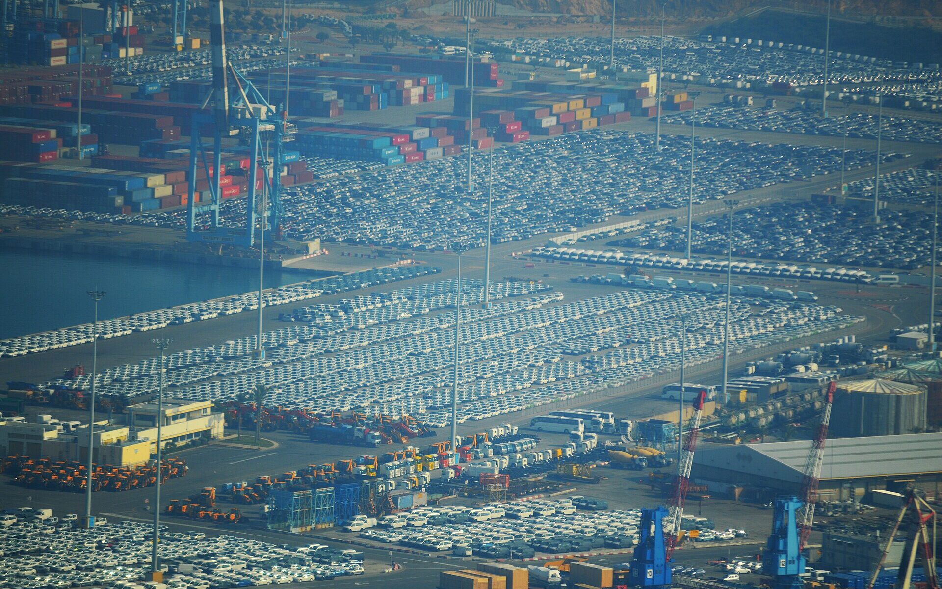 Aerial view of the quays at Ashdod Port covered in thousands of parked new cars, with container stacks, cranes and tour coaches