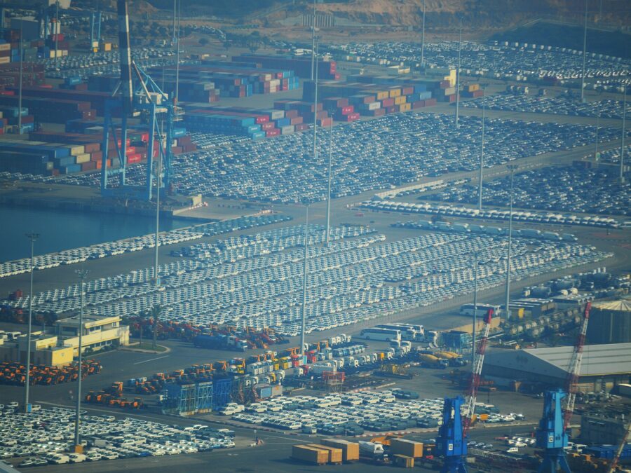 Aerial view of the quays at Ashdod Port covered in thousands of parked new cars, with container stacks, cranes and tour coaches