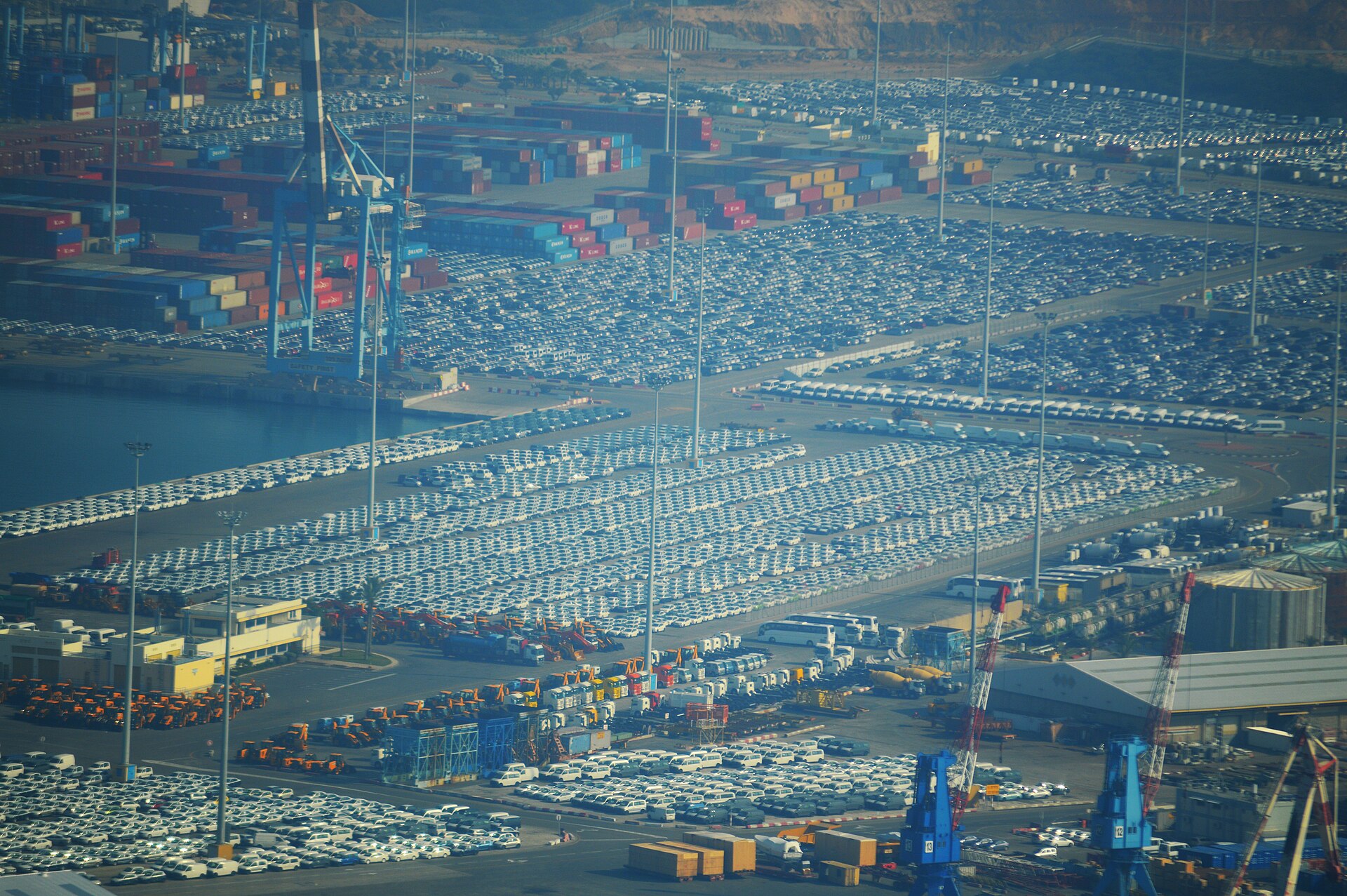 Aerial view of the quays at Ashdod Port covered in thousands of parked new cars, with container stacks, cranes and tour coaches