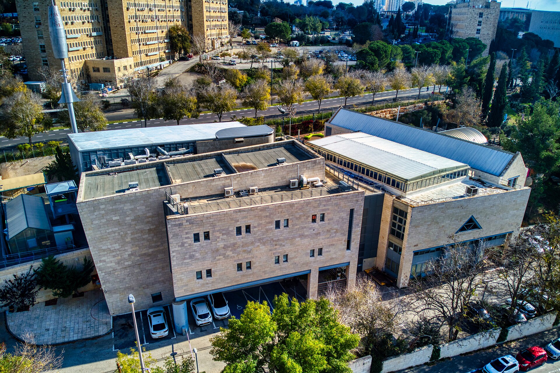 Aerial view of the Bloomfield Science Museum's stone buildings and glass-roofed hall on the Givat Ram campus in Jerusalem, with government office blocks behind