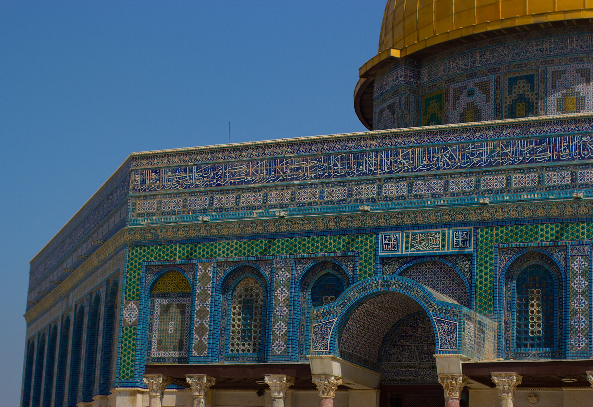 Blue, turquoise and green glazed tiles and a band of Quranic calligraphy on the Dome of the Rock's octagonal wall, with the gilded dome rising above