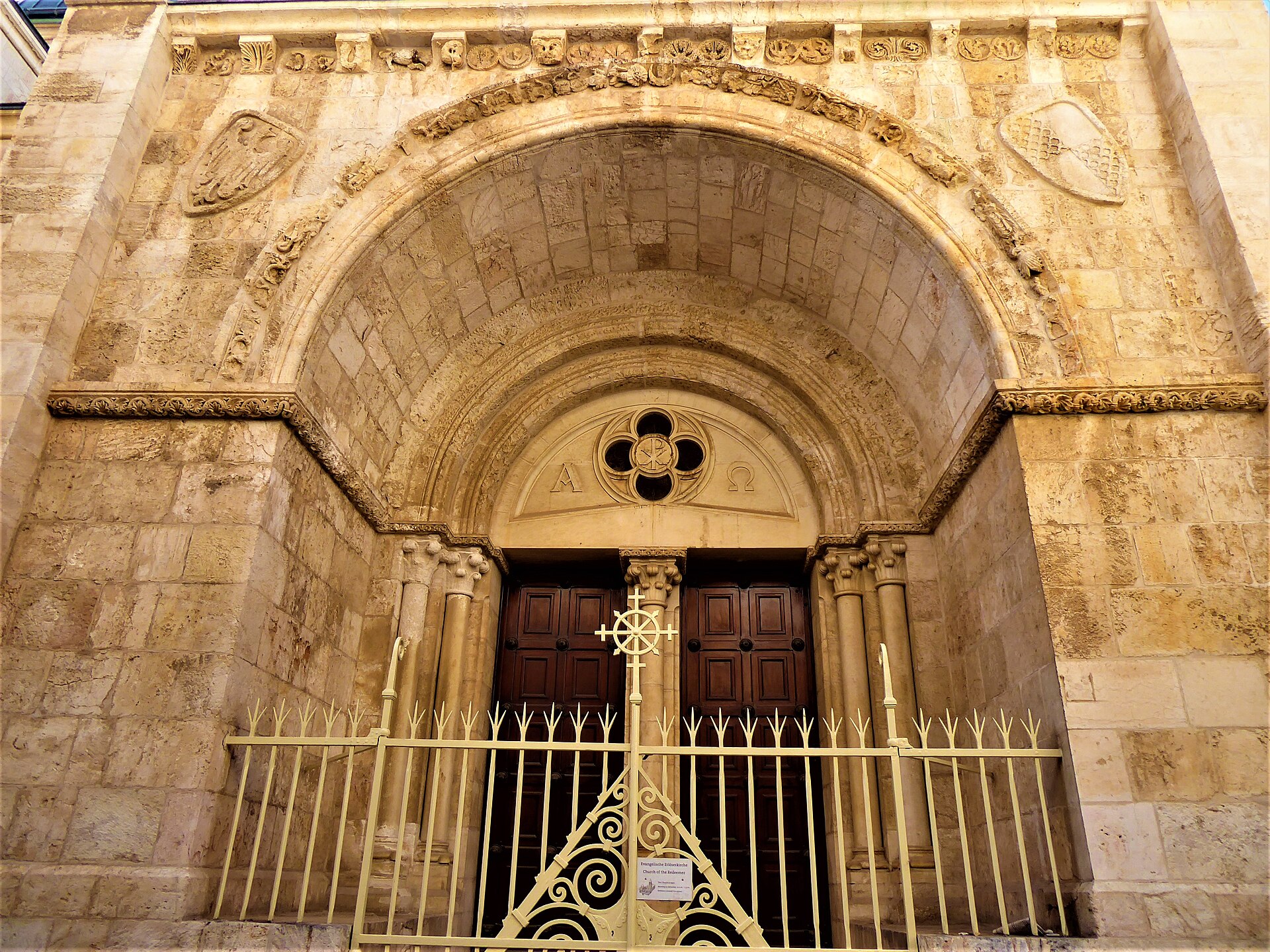 Carved Romanesque archway of the north portal of the Lutheran Church of the Redeemer in Jerusalem's Christian Quarter, with a medieval frieze above wooden doors and an iron gate