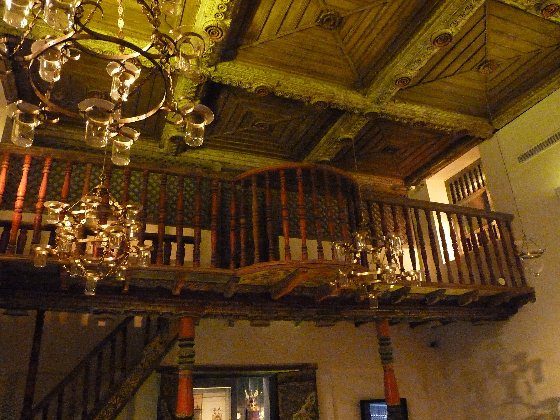 Carved wooden ceiling and balustraded women's gallery of the Cochin synagogue interior at the Israel Museum, hung with chandeliers of glass oil lamps