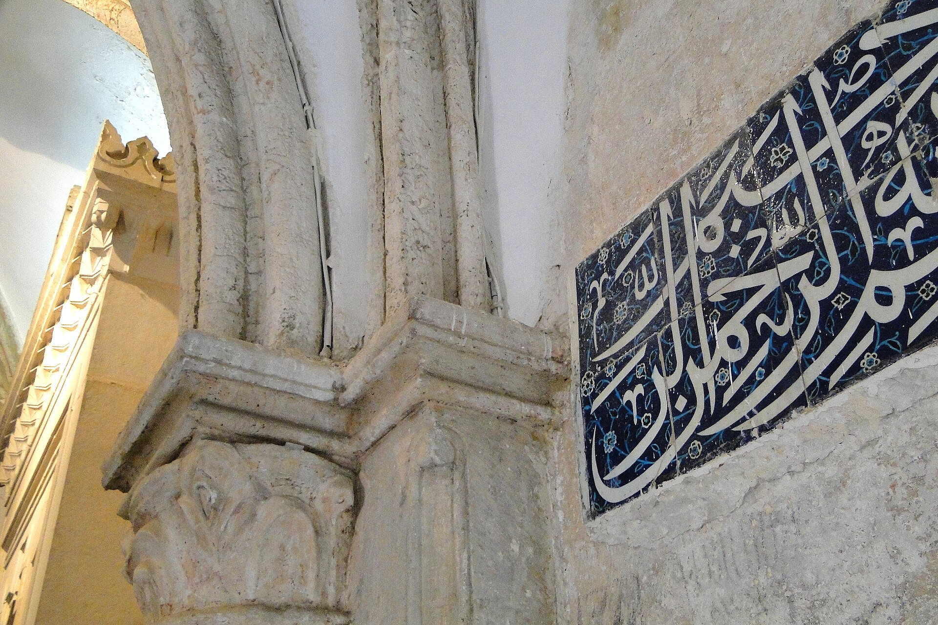 Detail inside the Room of the Last Supper, showing a carved Gothic column capital and ribbed arch beside a blue-and-white Ottoman tile panel with Arabic calligraphy