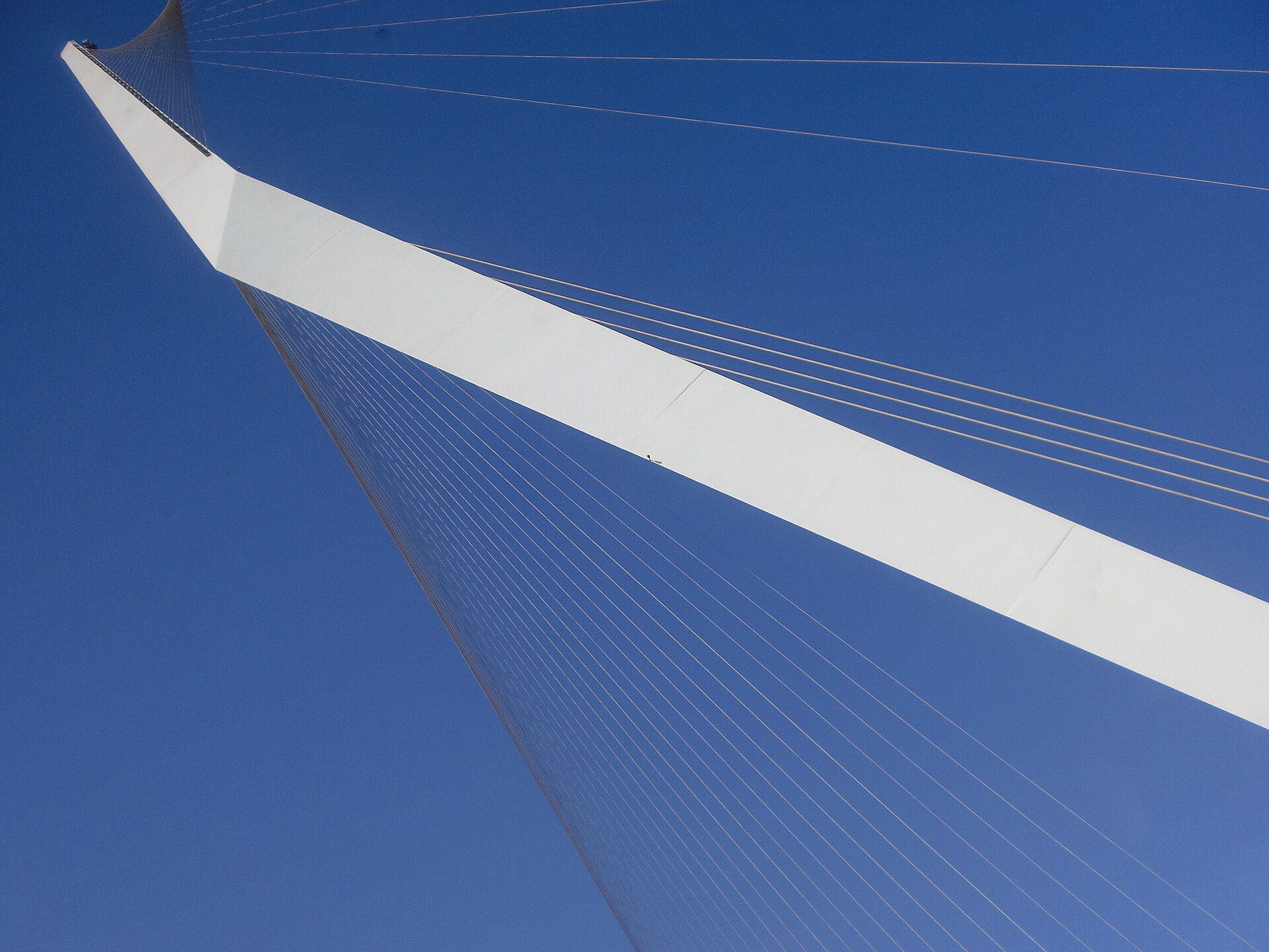 Looking up at the white pylon and fanned steel cables of the Chords Bridge against a deep blue sky