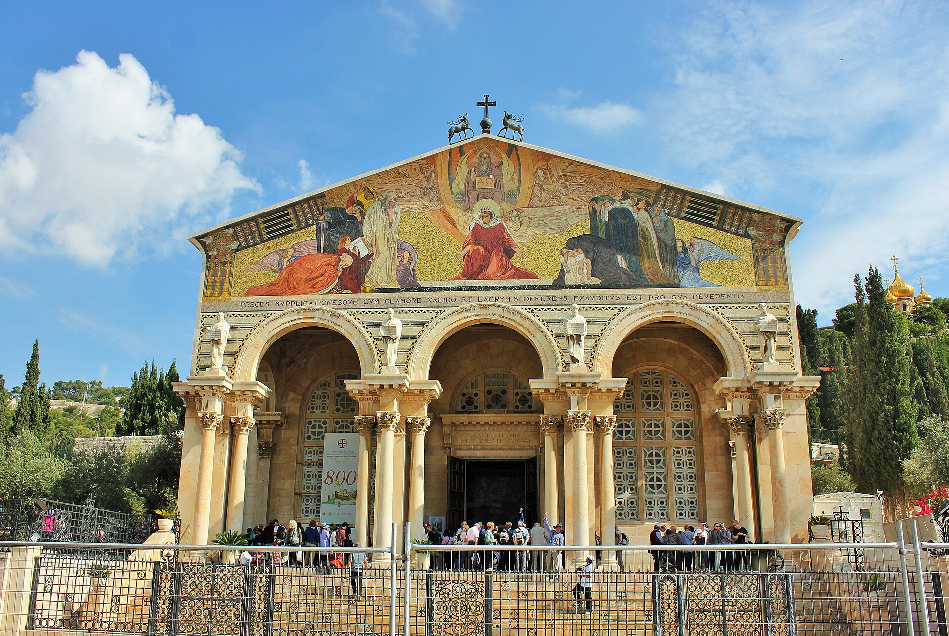 Church of All Nations facade at Gethsemane: a gold mosaic pediment over an arched portico whose columns carry statues of the four evangelists, with visitors below