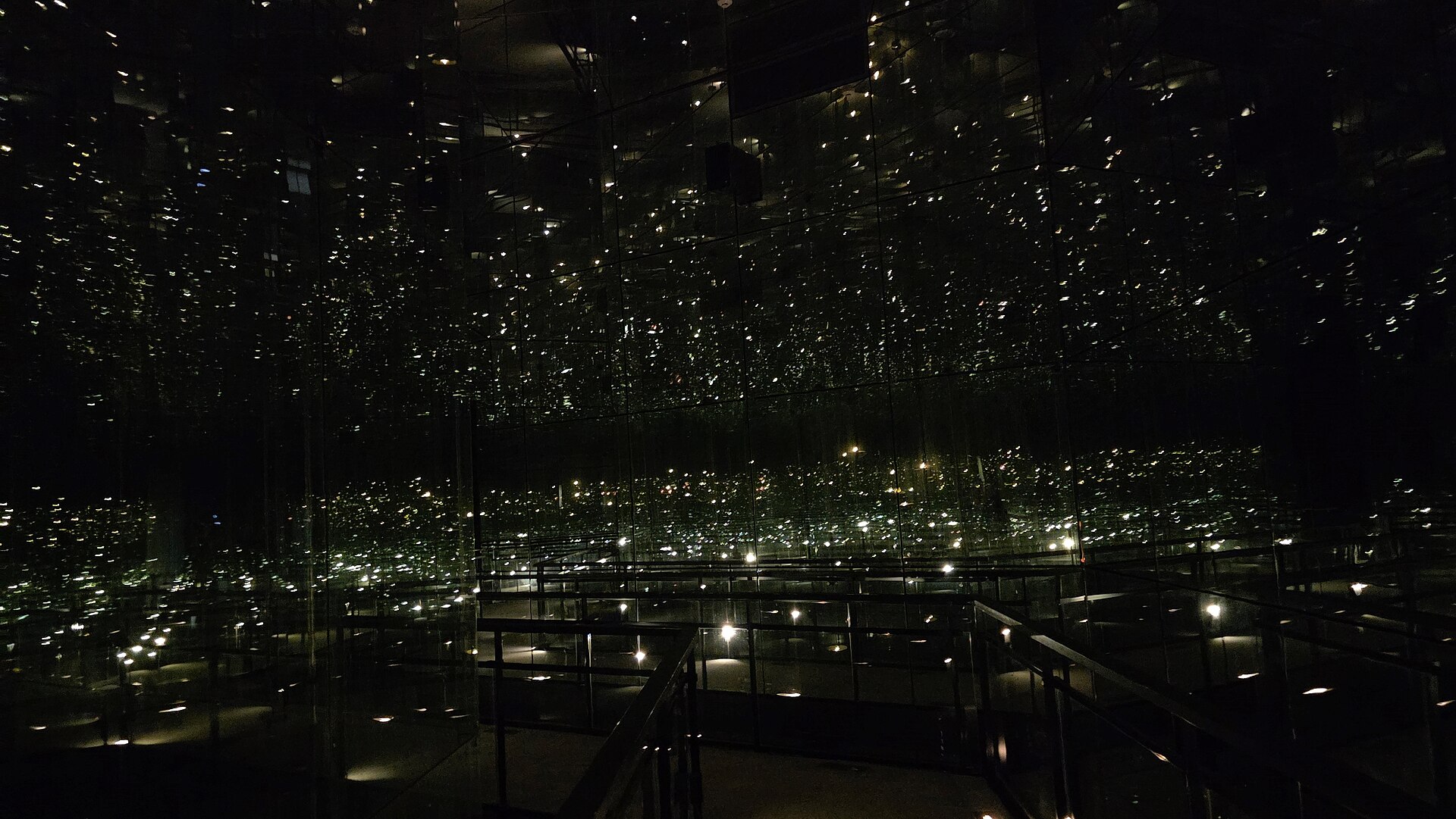 Dark mirrored hall of the Children's Memorial at Yad Vashem, where countless reflected candle flames look like stars around a railed walkway