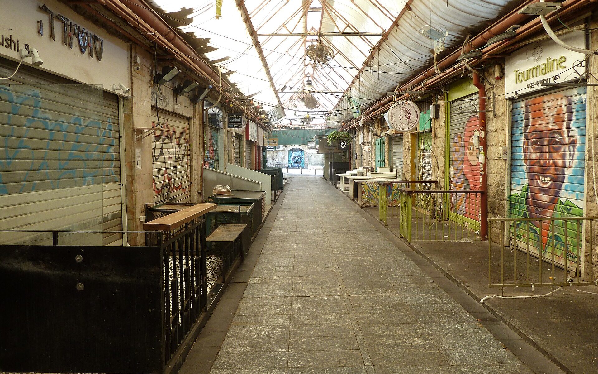 A deserted covered lane of Mahane Yehuda market in Jerusalem on a Saturday morning, every stall shuttered and several shutters painted with murals