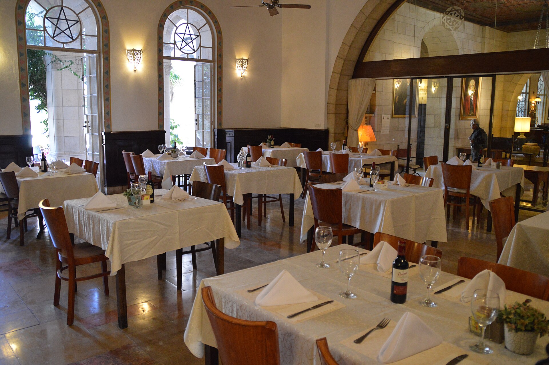 Dining room of the restaurant inside the Jerusalem International YMCA, with white-clothed tables set with wine glasses beneath tall arched windows