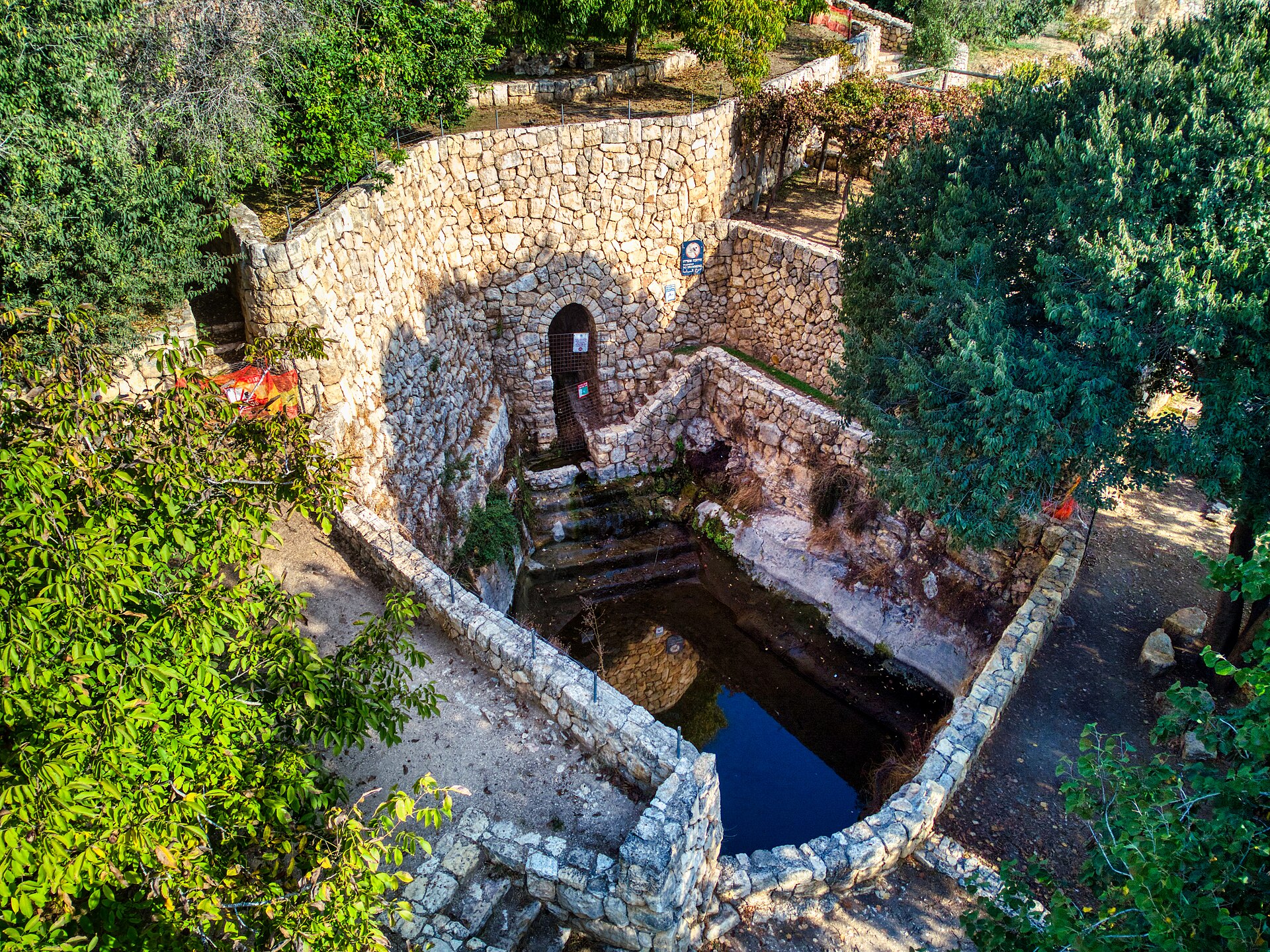 Ein Bikura spring at Sataf, a stone-walled pool with steps down to the water fed from an arched tunnel entrance, surrounded by terraces and trees