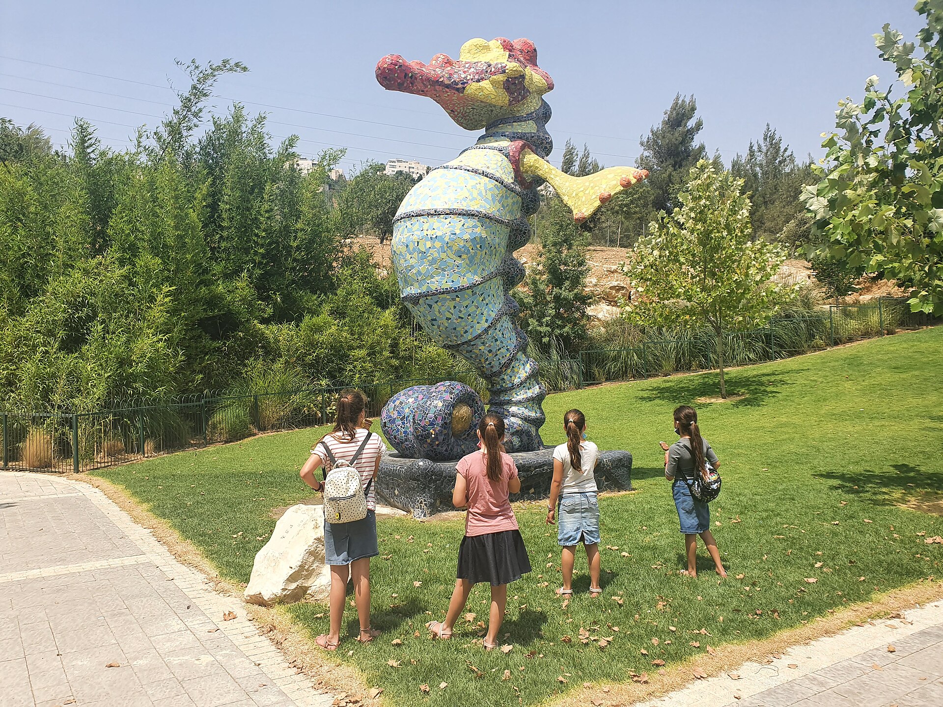 Four girls seen from behind stand on a lawn looking up at a giant colourful mosaic seahorse sculpture in the gardens of the Israel Aquarium