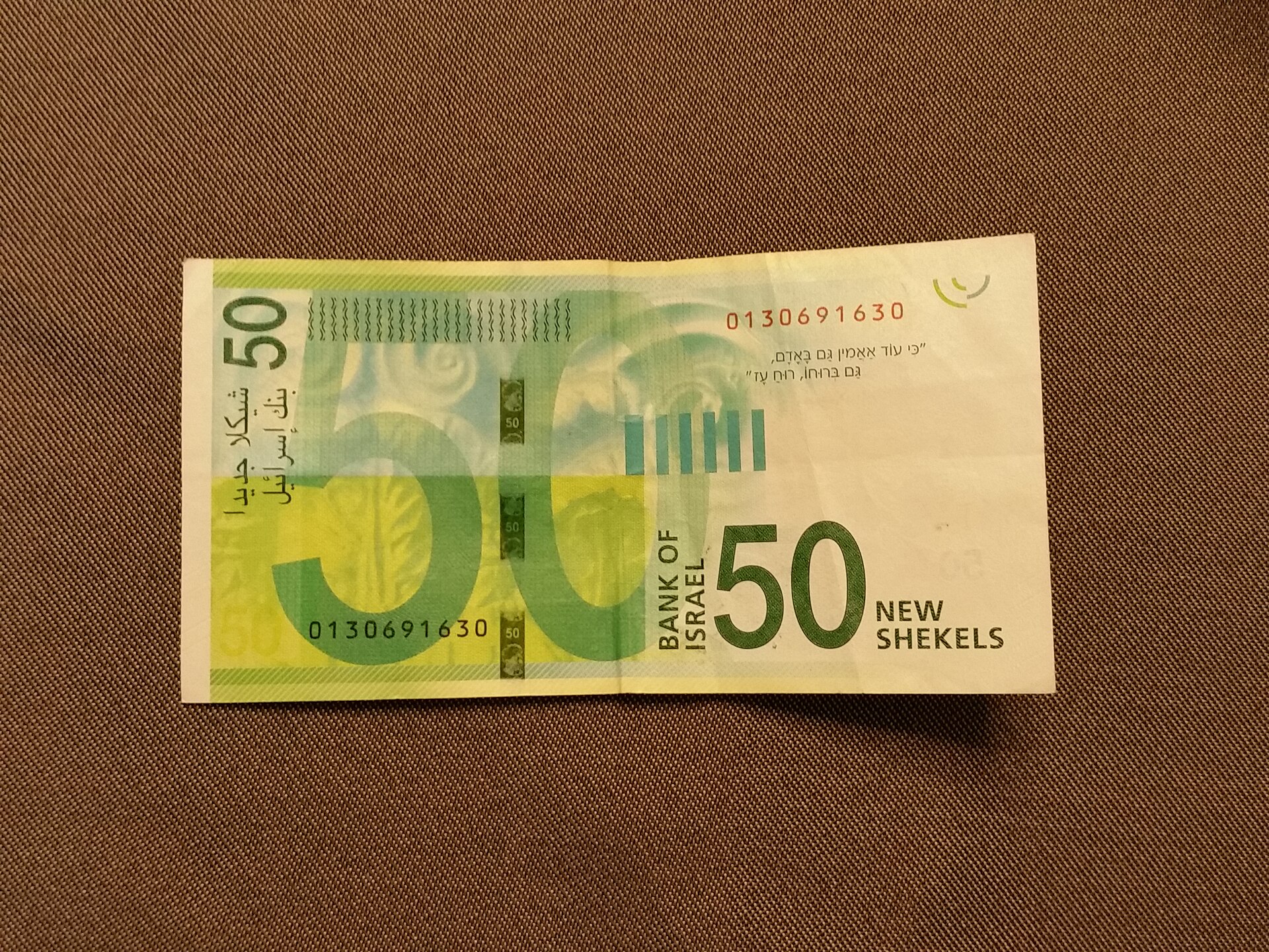 Green Israeli 50 new shekel banknote of the current series lying on brown fabric, showing the Bank of Israel lettering, the large 50 and serial numbers
