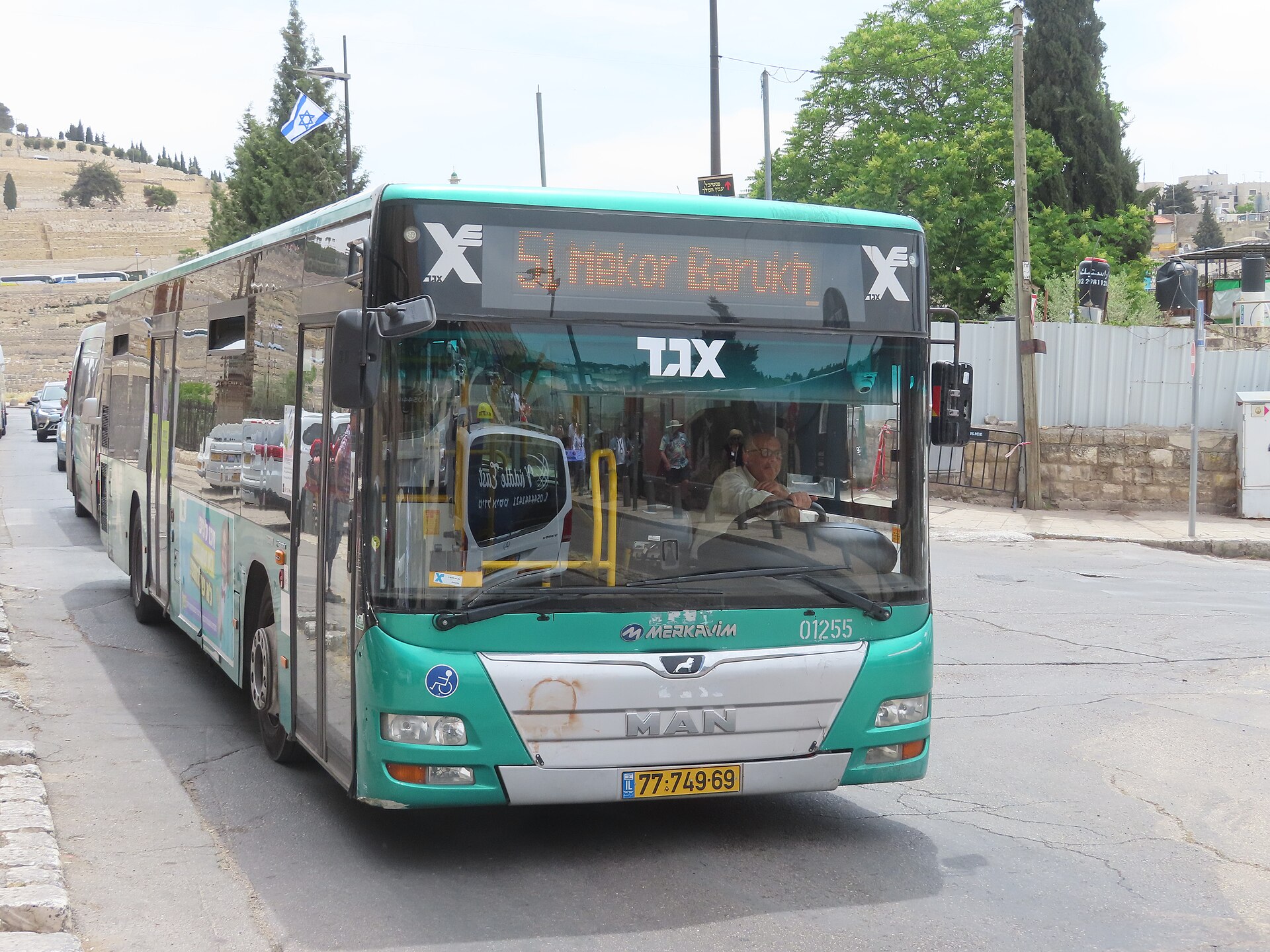 Green and white Egged city bus showing route 51 to Mekor Barukh on its destination display, driving along a Jerusalem street with a hillside cemetery behind