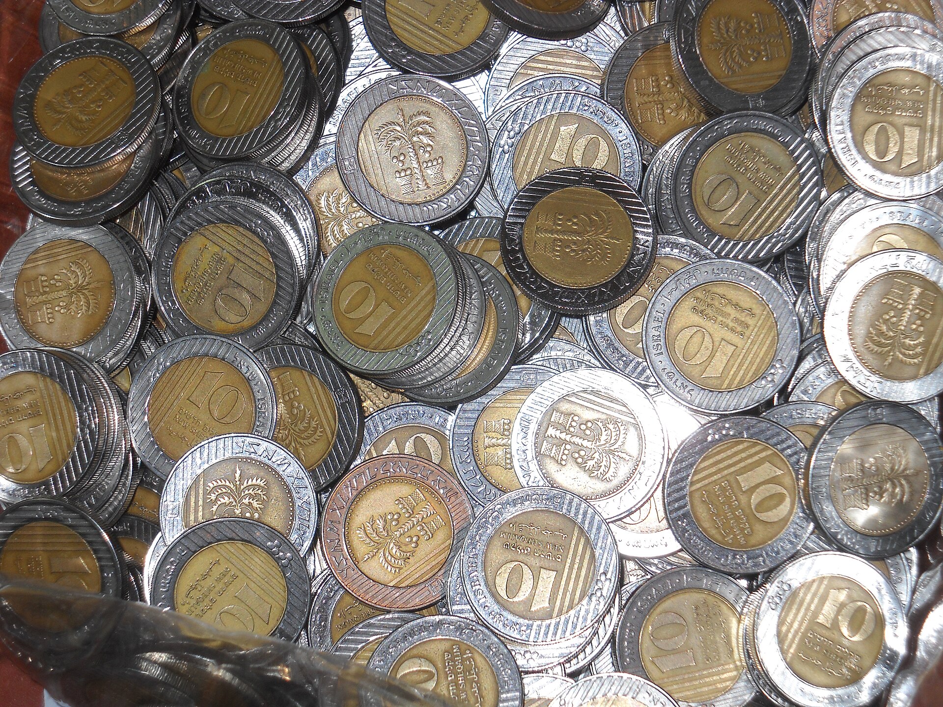 A heap of bimetallic Israeli 10-shekel coins with gold-coloured centres and silver rings, some showing a palm tree and others the numeral 10