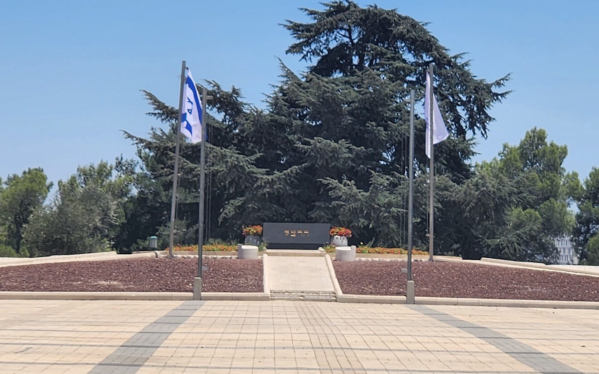 Theodor Herzl's tomb at the head of the paved ceremonial plaza on Mount Herzl, with Israeli flags and a large cedar behind