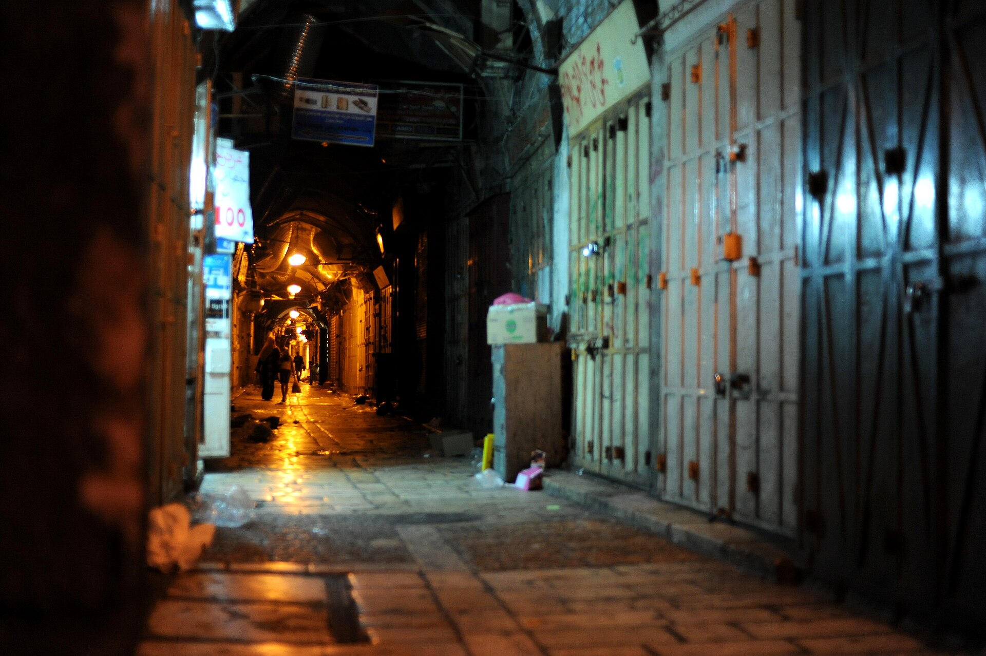 A shuttered, empty souq lane in the Old City of Jerusalem lit by hanging lamps late at night
