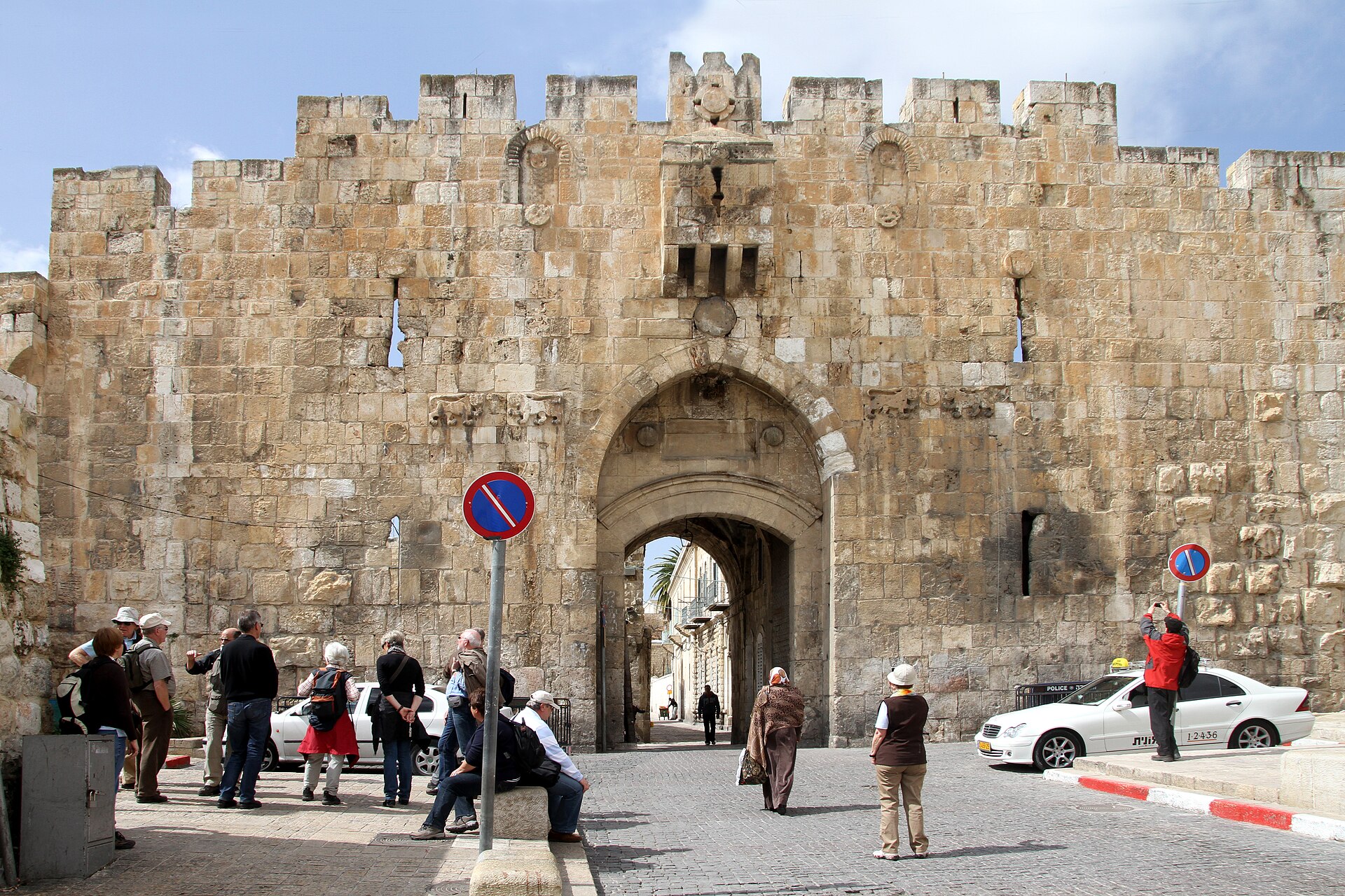 Lions' Gate in Jerusalem's eastern Old City wall, with pairs of carved lions flanking its arch, crenellations above and a group of tourists gathered in front