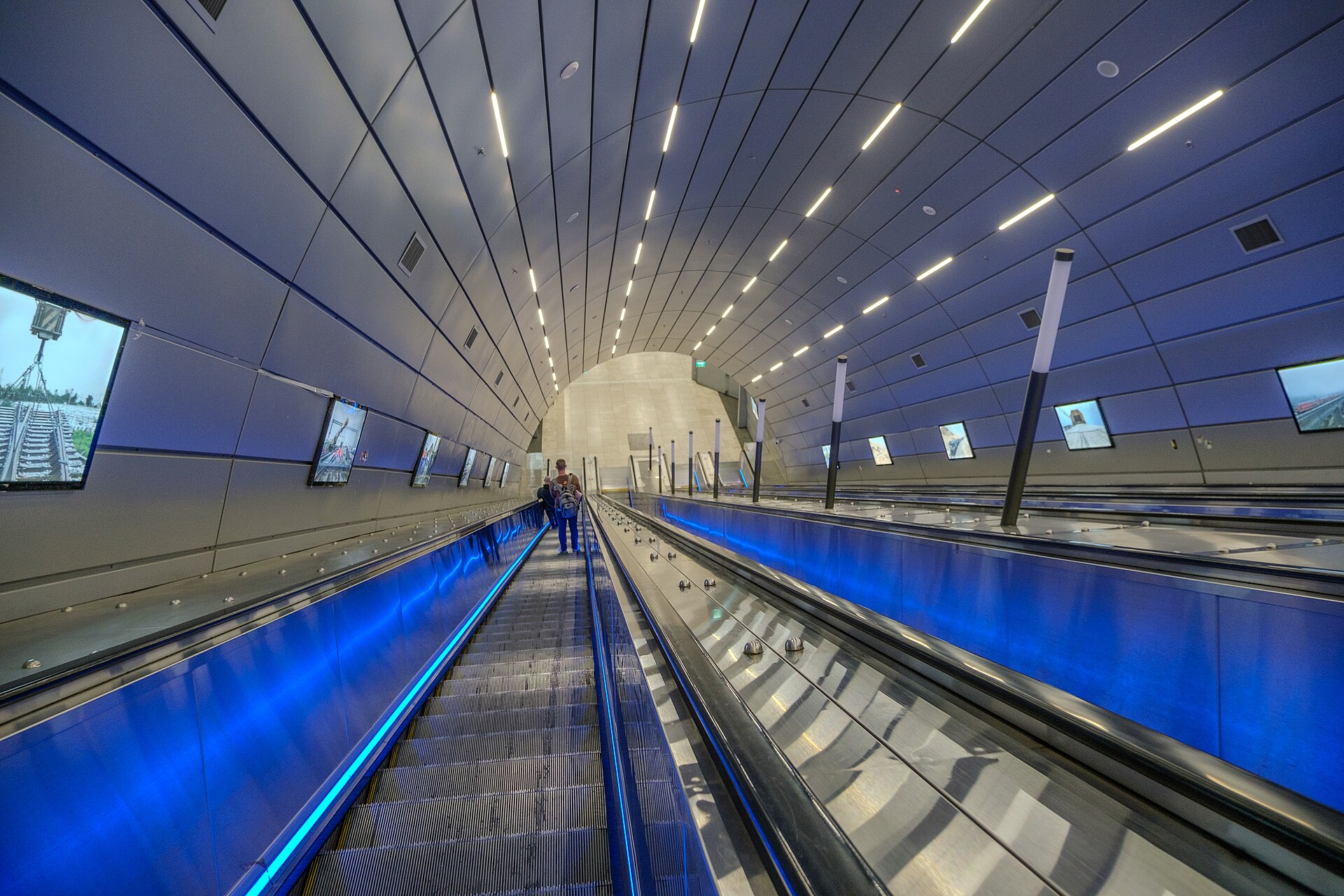Long banks of escalators with blue lighting under a curved, ribbed ceiling lead down to the deep platforms of Jerusalem–Yitzhak Navon railway station