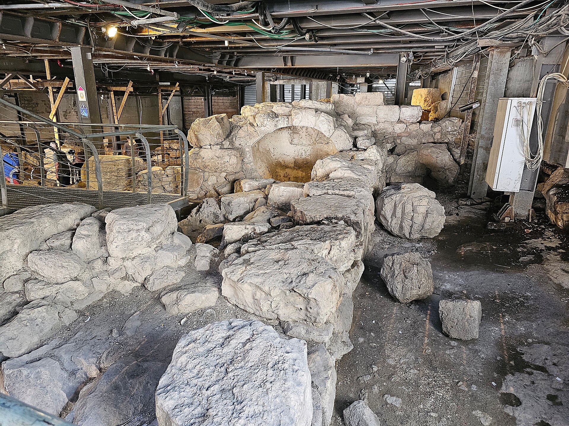 Massive ancient limestone walls and fallen blocks of the Large Stone Structure, excavated beneath a steel roof in the City of David, beside a visitor walkway