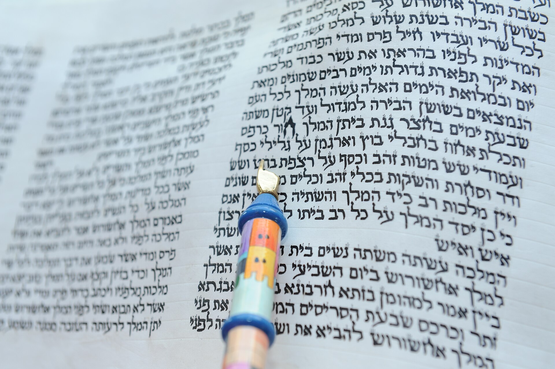 A hand-lettered Megillat Esther scroll with a decorated silver pointer resting on the Hebrew text