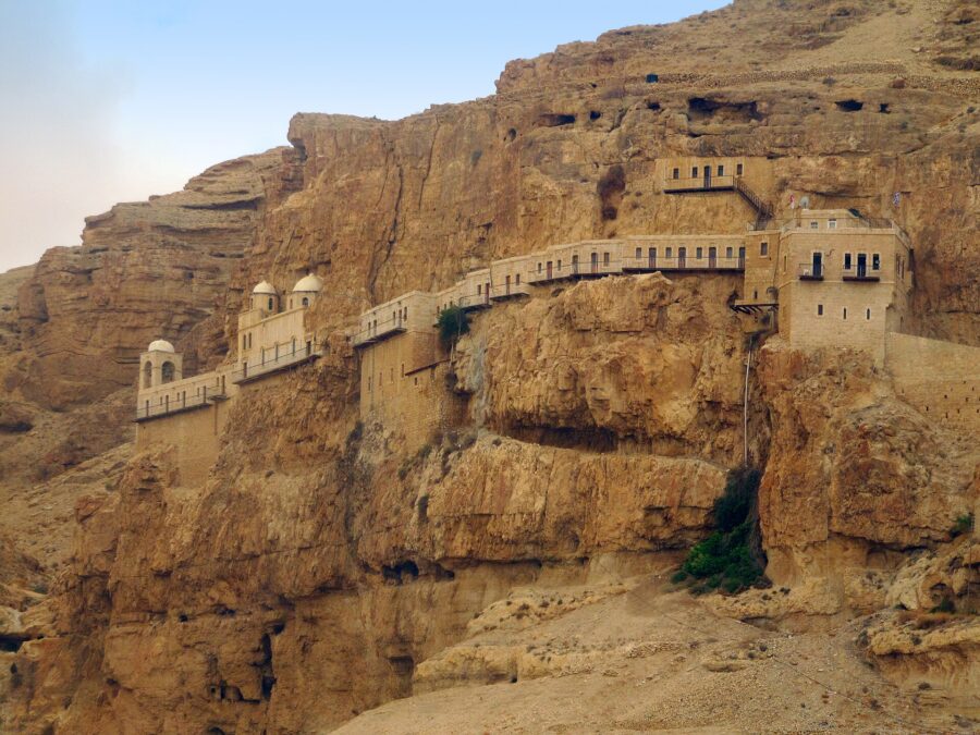 The Monastery of the Temptation, a long line of pale stone buildings with small domes and balconies built along a sheer ochre cliff face above Jericho