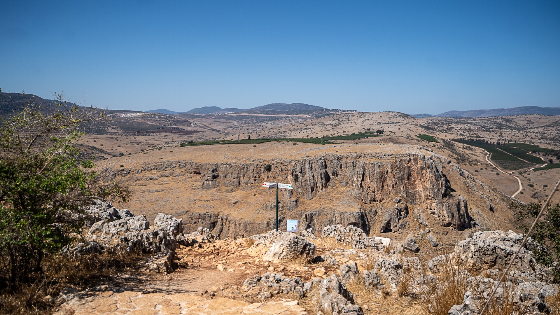 The limestone cliffs of Mount Arbel, west of the Sea of Galilee, with a hiking signpost in the foreground and the rolling hills of Lower Galilee beyond
