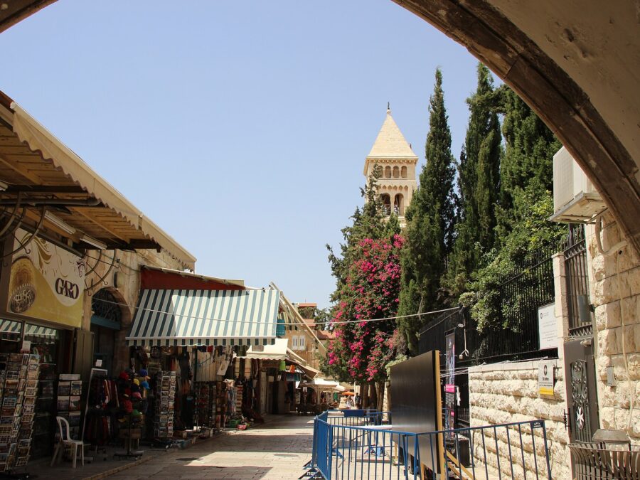 Muristan Road in Jerusalem's Christian Quarter framed by a stone arch, with souvenir shops, cypress trees and the Church of the Redeemer bell tower