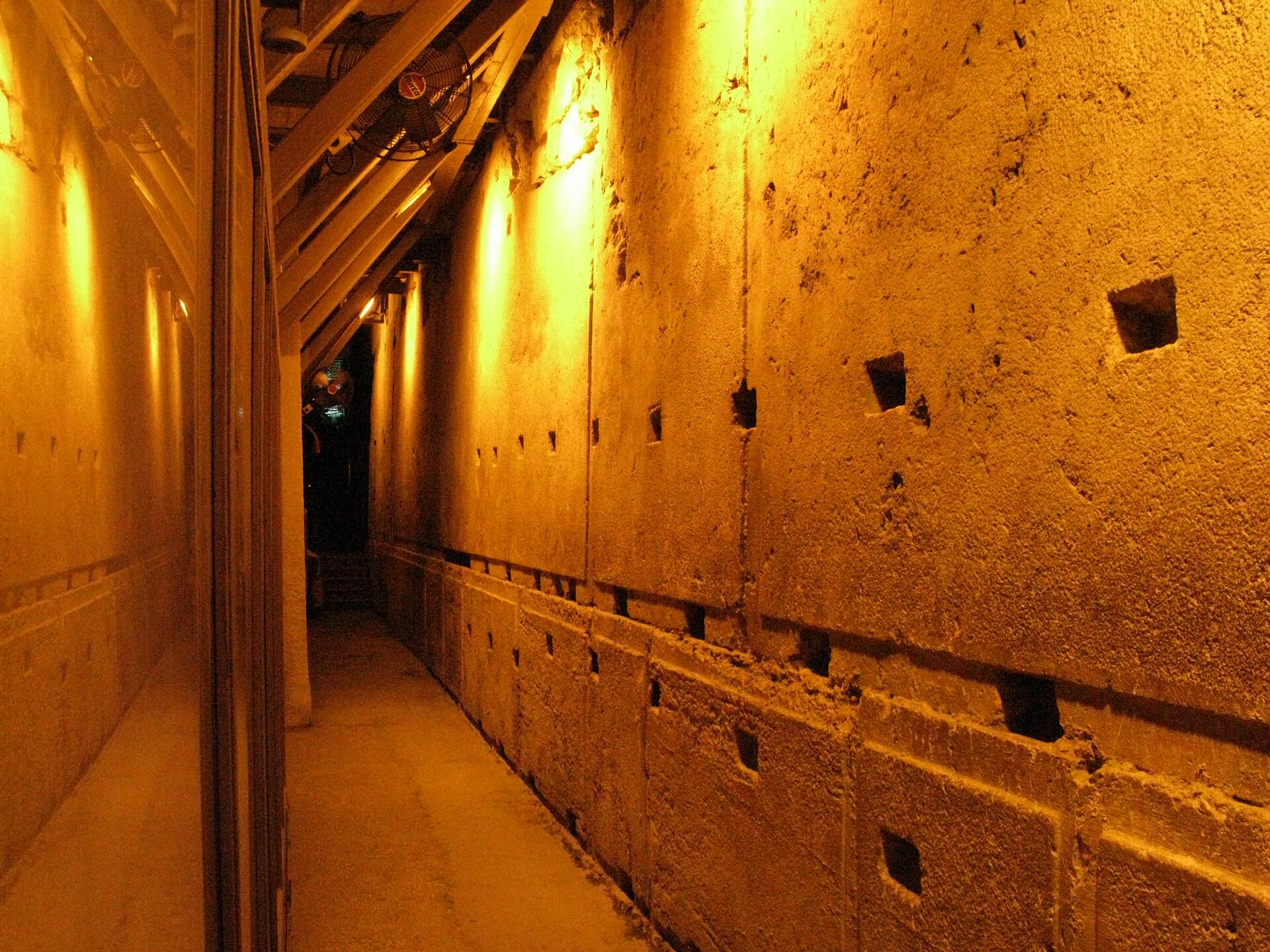 A narrow passage in the Western Wall Tunnels runs beside enormous Herodian ashlars with drafted margins, lit by warm lamps under sloping steel beams