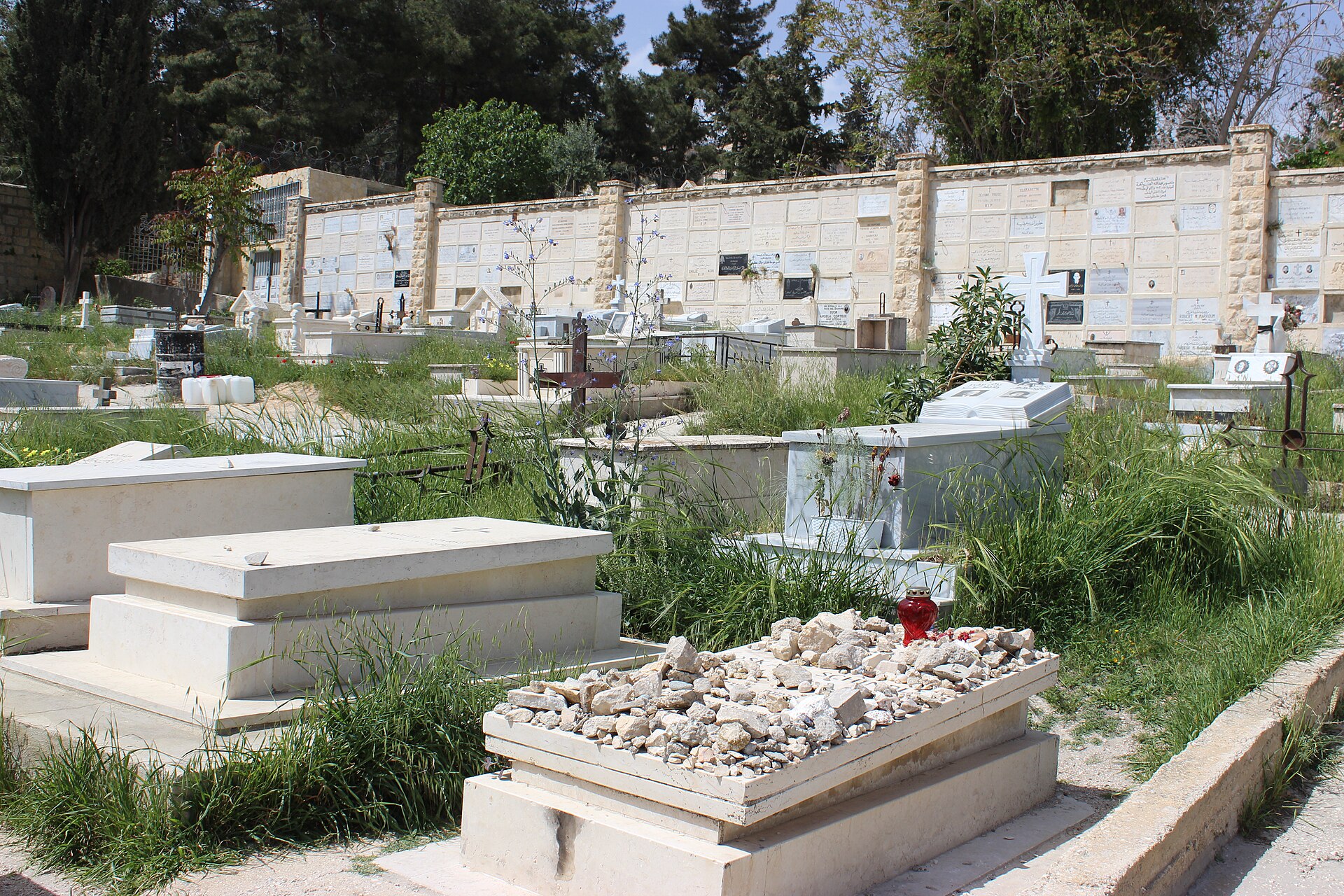 Graves in the Franciscan cemetery on Mount Zion, with a plain stone grave in the foreground heaped with small pebbles and a red candle holder