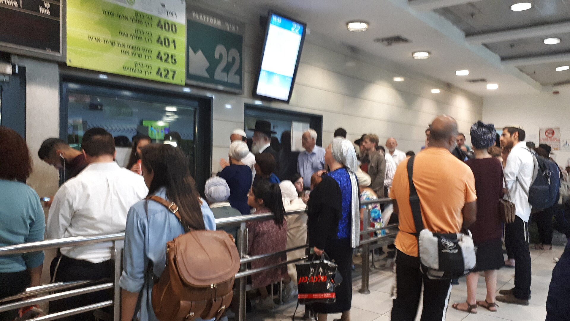 Passengers queueing at an intercity platform inside Jerusalem Central Bus Station beneath an electronic departure sign