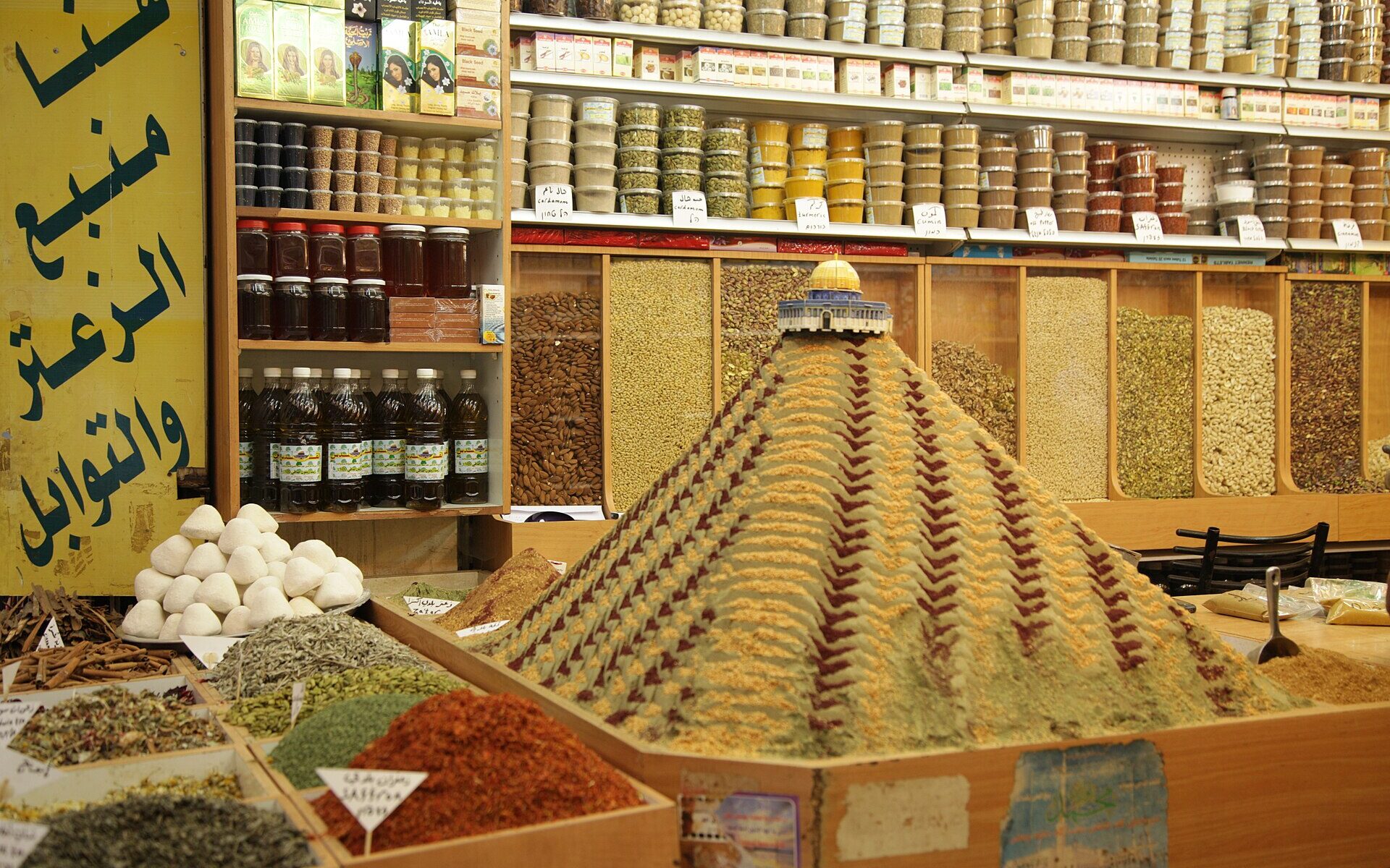 A patterned pyramid of ground spices topped by a model of the Dome of the Rock in an Old City spice shop, with shelves of labelled spice tubs behind