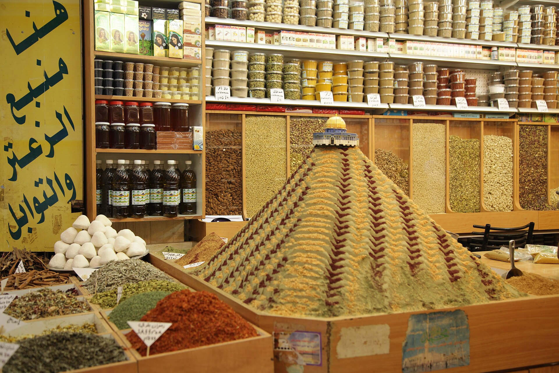 A patterned pyramid of ground spices topped by a model of the Dome of the Rock in an Old City spice shop, with shelves of labelled spice tubs behind