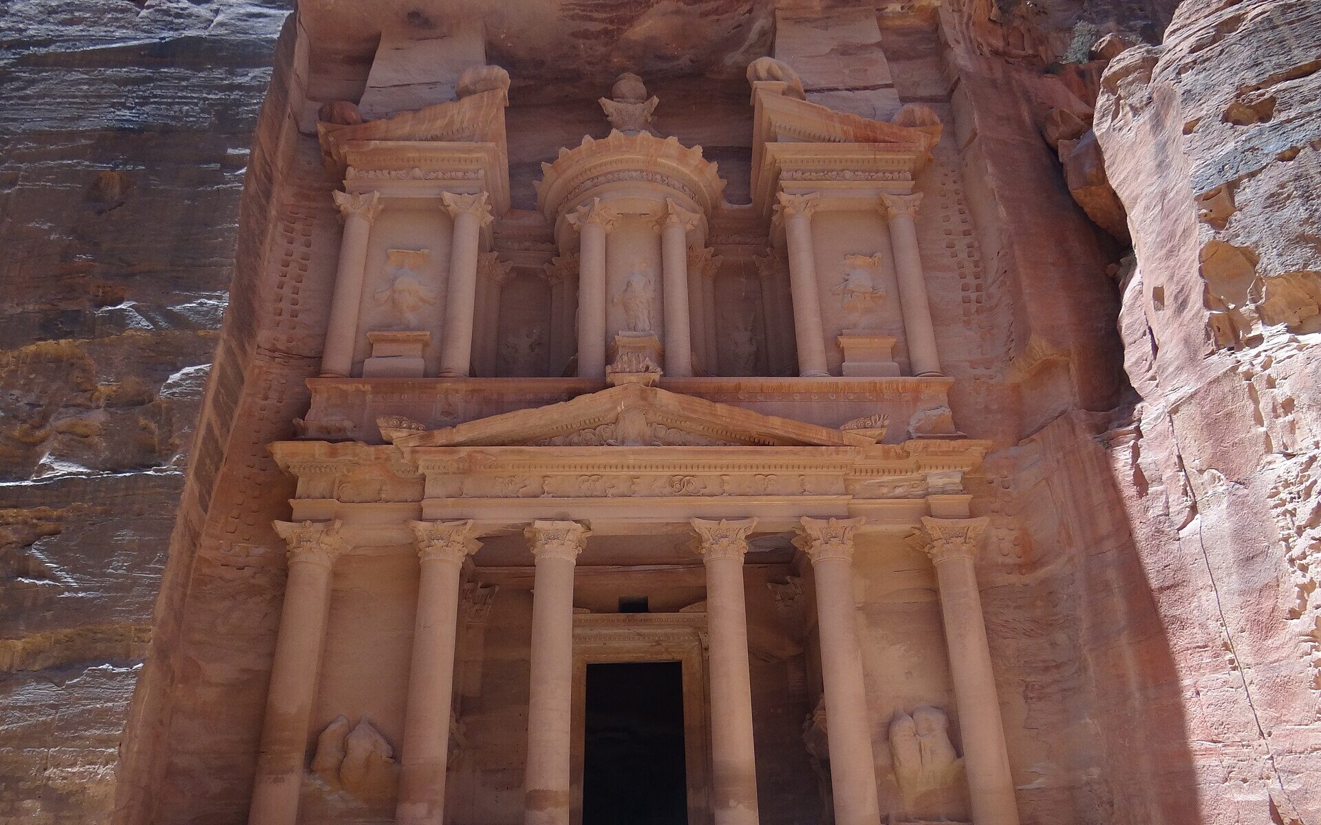 The rose-red carved facade of Al-Khazneh, the Treasury, at Petra in Jordan, with columns, pediments and statues cut into the sandstone cliff