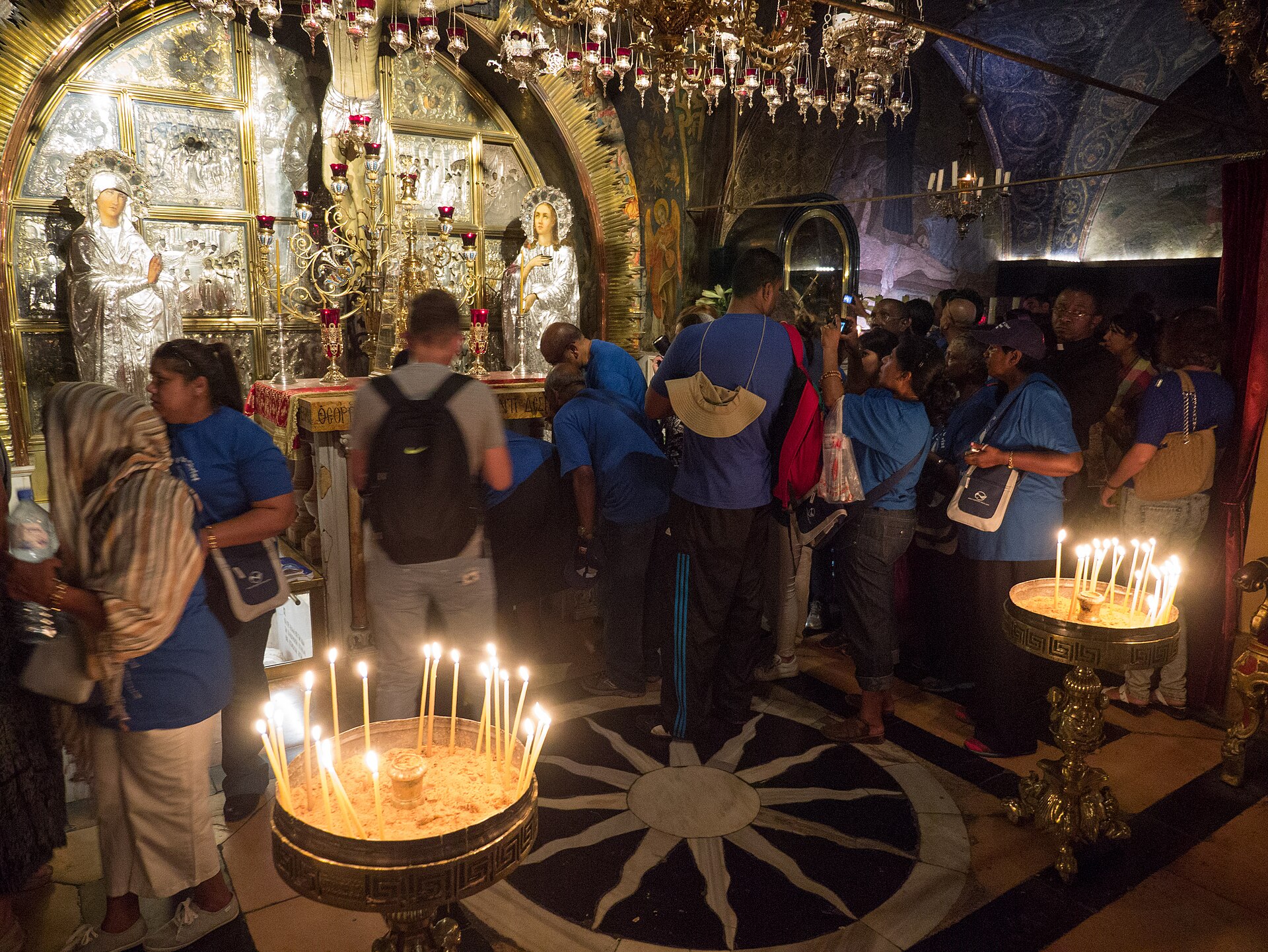 Pilgrim group in matching blue T-shirts waiting to kneel at the Greek Orthodox altar on Golgotha, inside the Church of the Holy Sepulchre, beside stands of lit candles