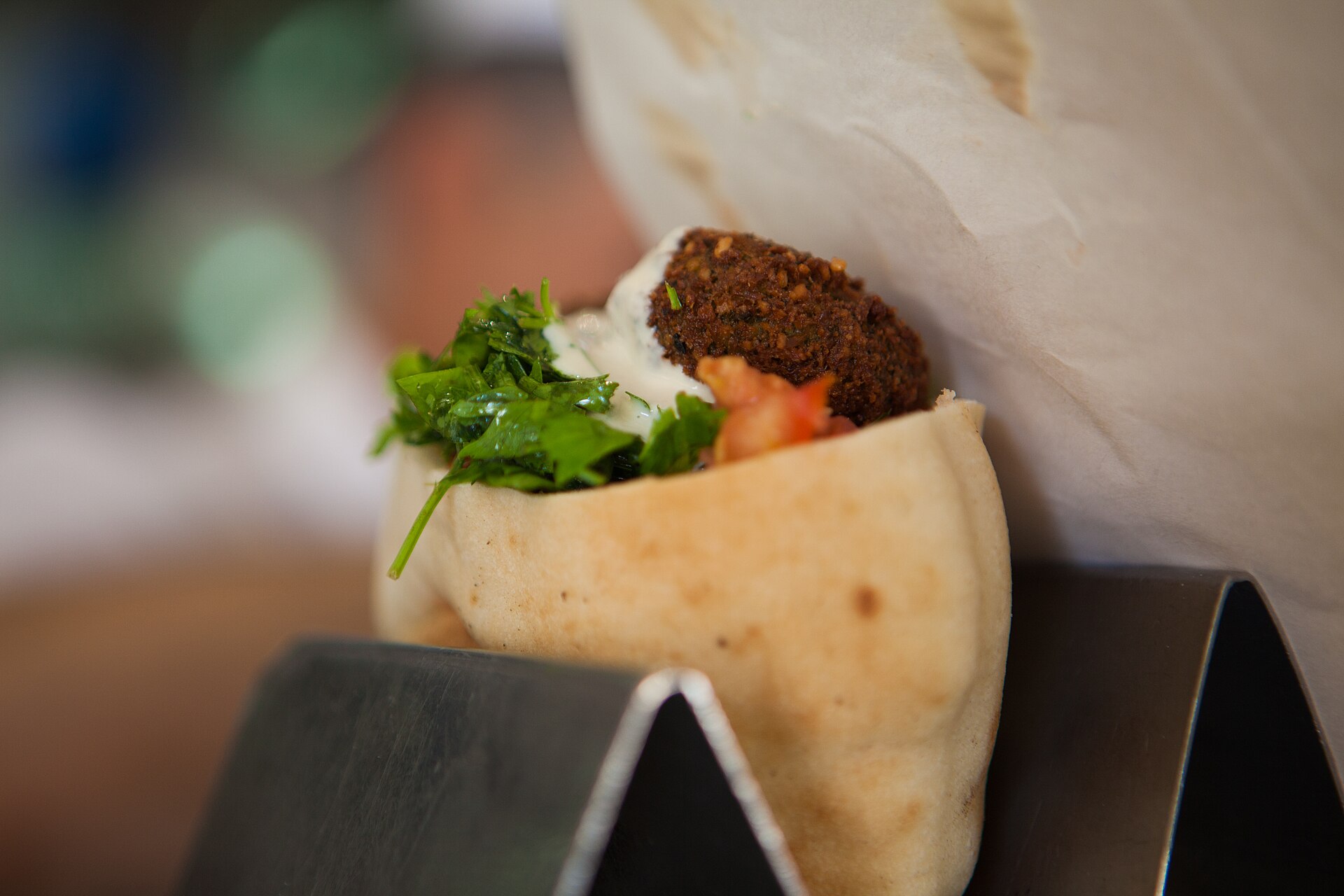 Pita stuffed with a crisp falafel ball, chopped parsley, diced tomato and a drizzle of tahini, standing in a metal pita holder