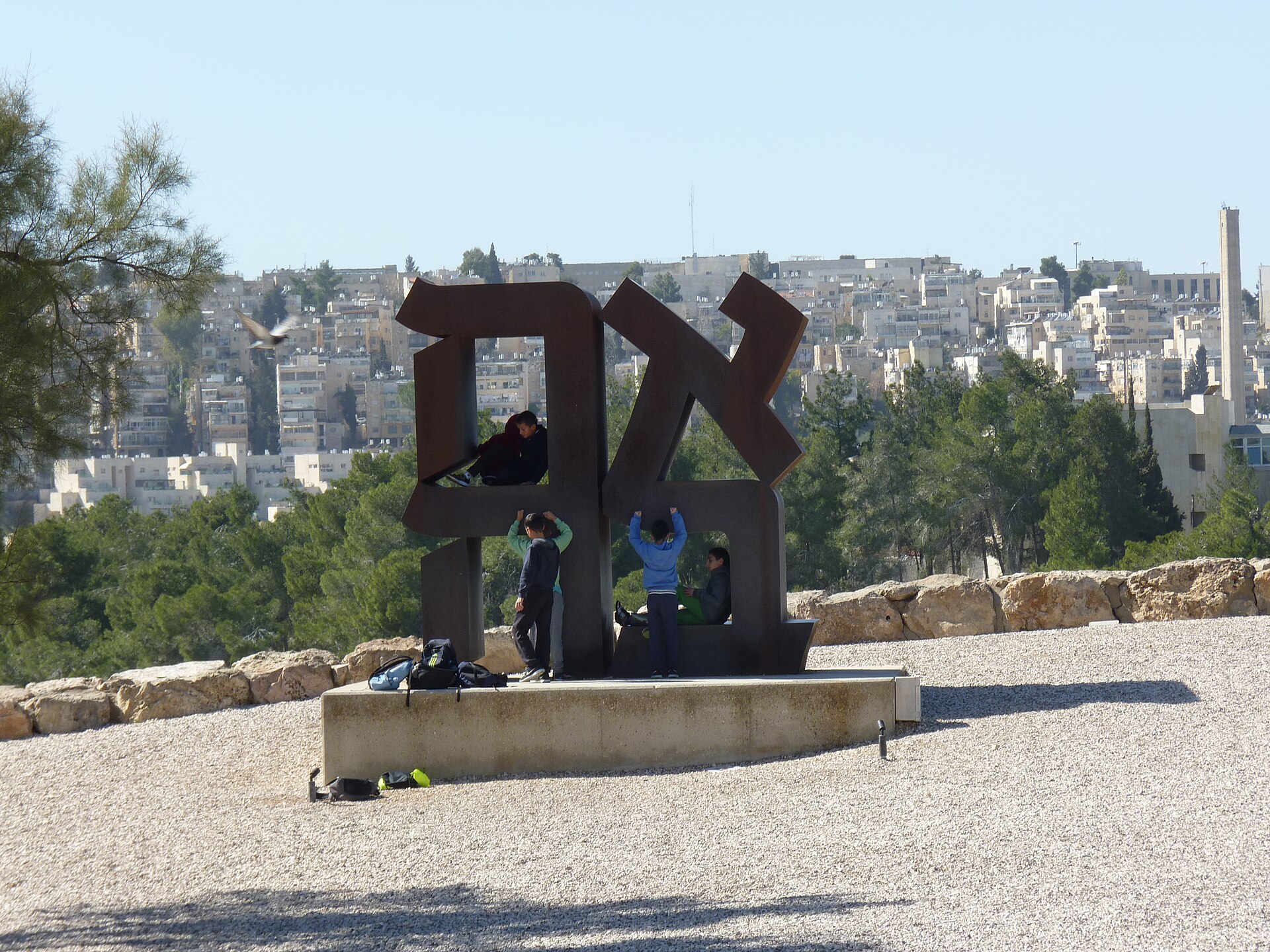 Robert Indiana's rust-brown steel AHAVA sculpture, the Hebrew word for love, on a gravel terrace of the Billy Rose Art Garden, with children playing among its letters