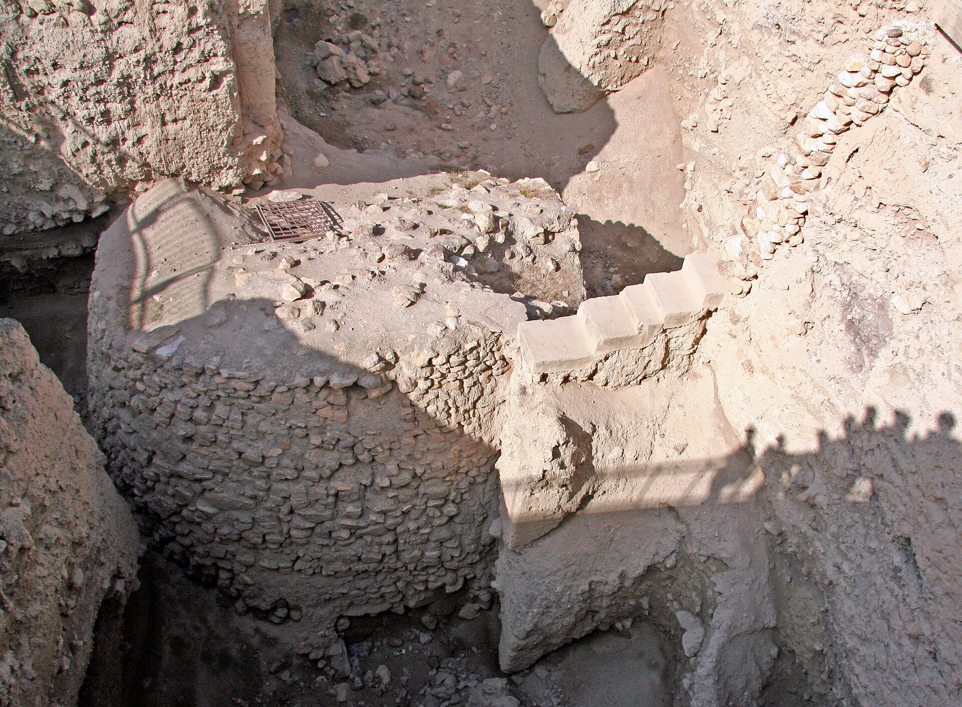 The round Neolithic stone tower of Jericho at Tel es-Sultan, seen from above in a deep excavation trench with a small grille on top and modern steps alongside