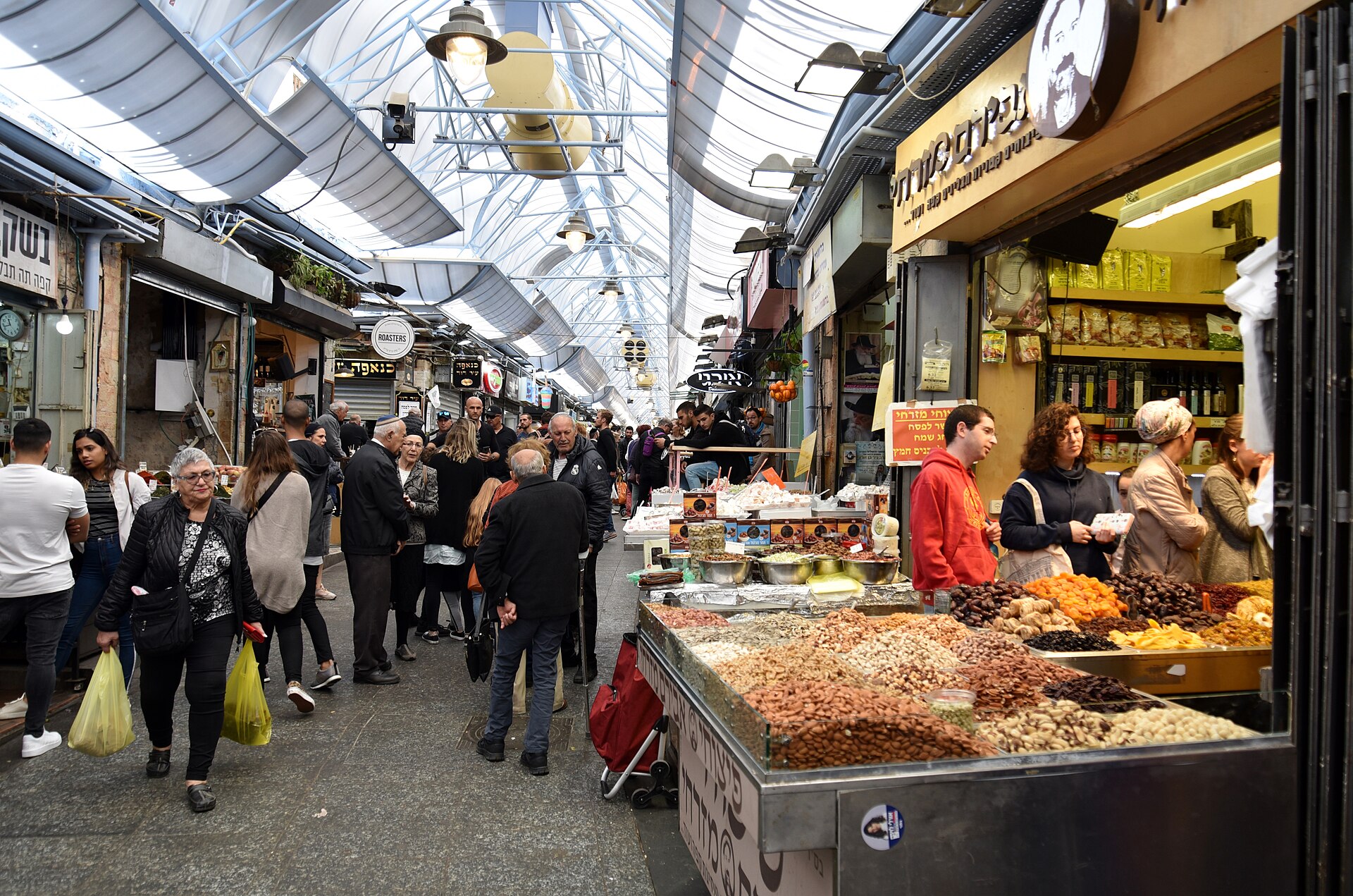 Shoppers pass a nut and dried fruit stall in a covered lane of Mahane Yehuda Market, where a Hebrew sign announces the goods are kosher for Passover