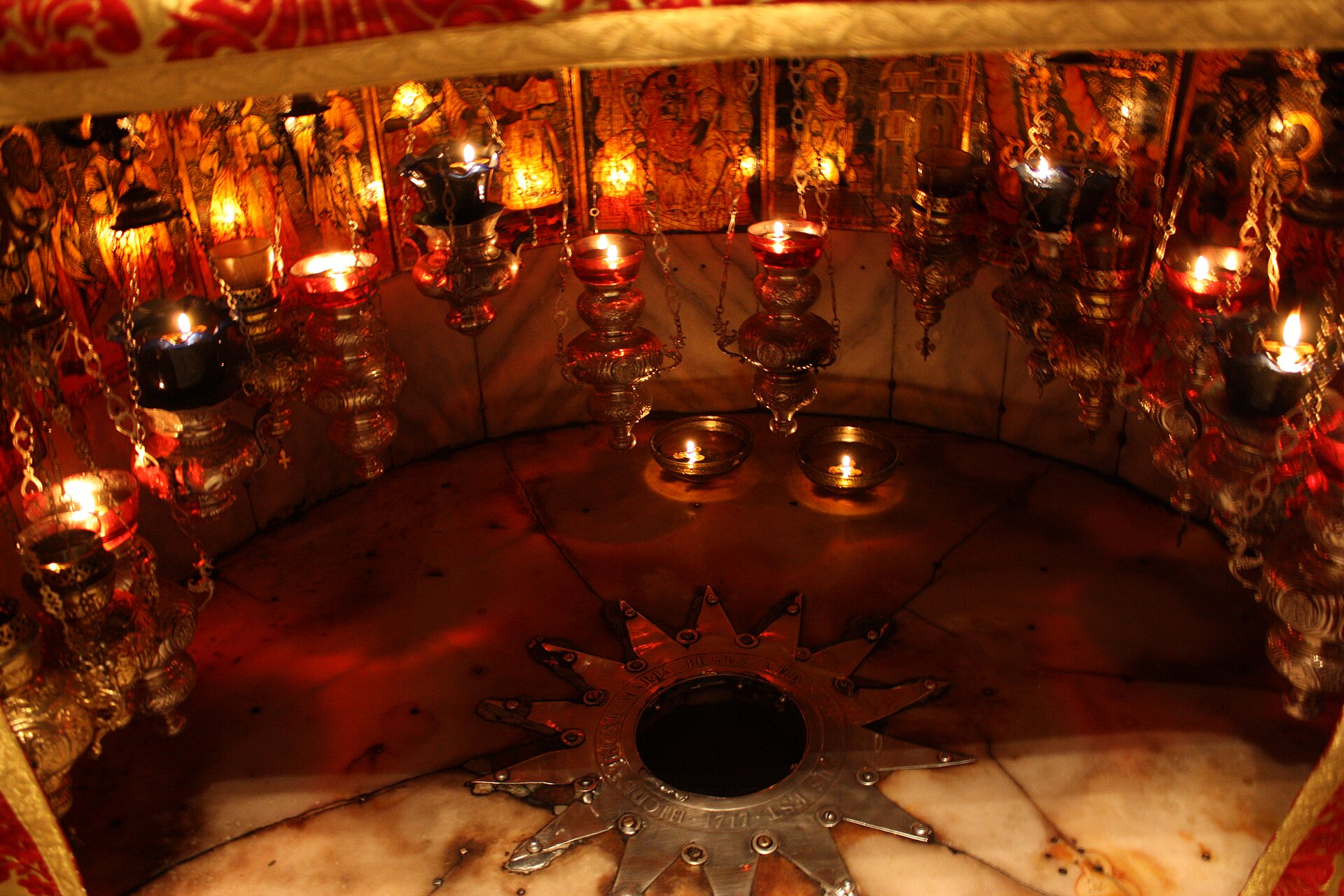 A silver fourteen-pointed star set into marble beneath hanging oil lamps in the Grotto of the Nativity