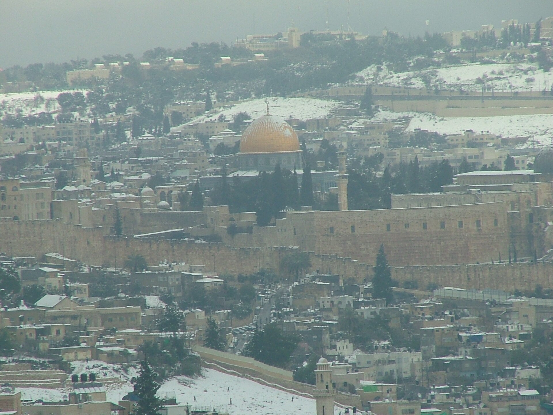 Snow on the rooftops below Jerusalem's Old City walls and the golden Dome of the Rock, with the Mount of Olives dusted white behind