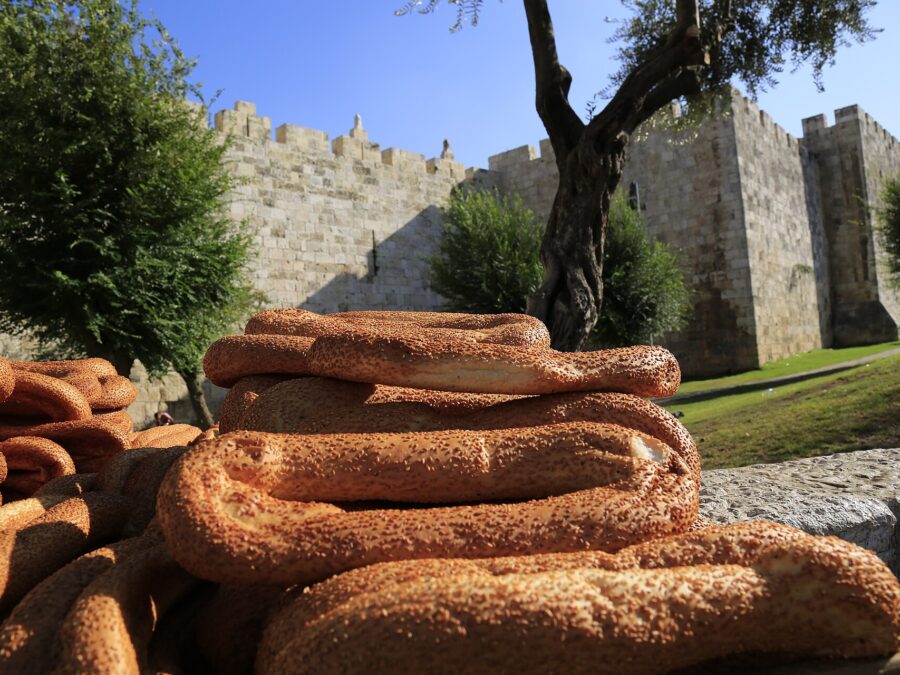 Stacks of sesame-crusted ka'ak bread in the foreground, with the crenellated stone walls of Jerusalem's Old City and an olive tree behind