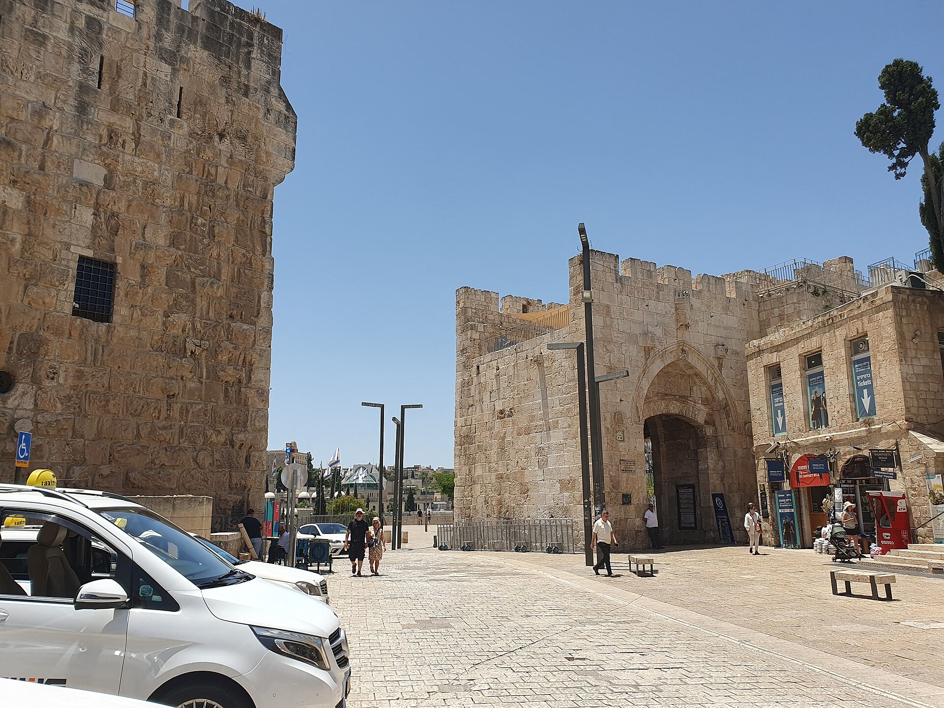 Taxis parked in the square just inside Jaffa Gate beside the Tower of David citadel, with the gate's pointed inner arch and the road breach in the wall beyond