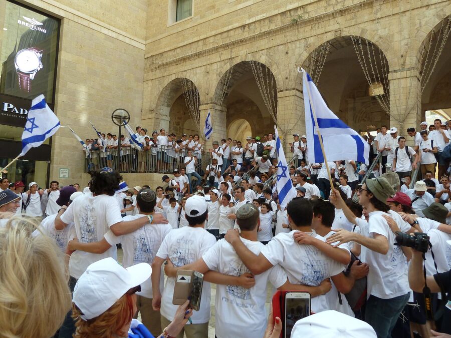 Teenagers in white T-shirts dance arm in arm and wave Israeli flags beneath the stone arcades of Mamilla, just outside the Old City, on Jerusalem Day