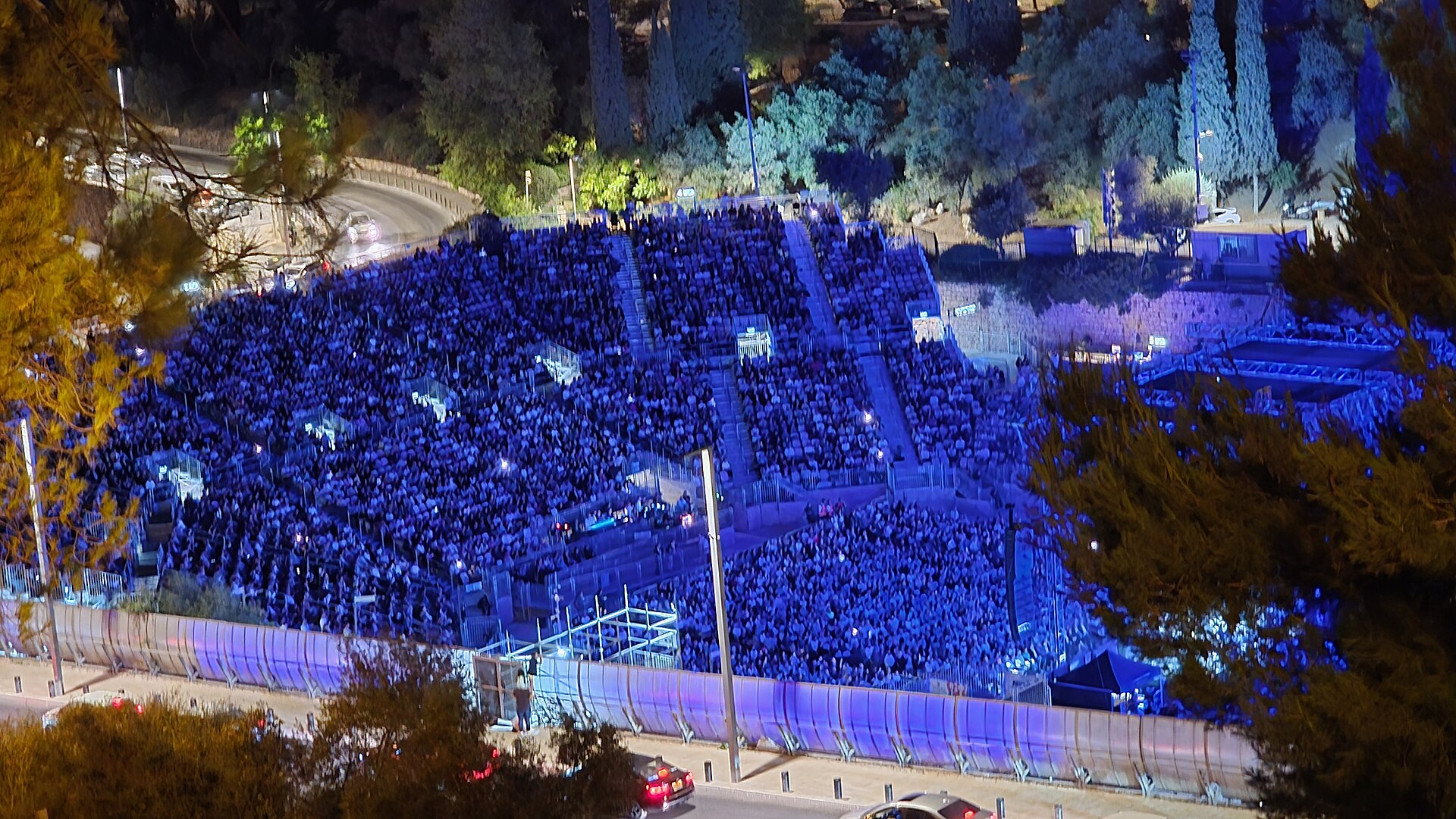 Thousands of spectators bathed in blue stage light fill the tiered seating of the Sultan's Pool amphitheatre during a summer night concert in Jerusalem