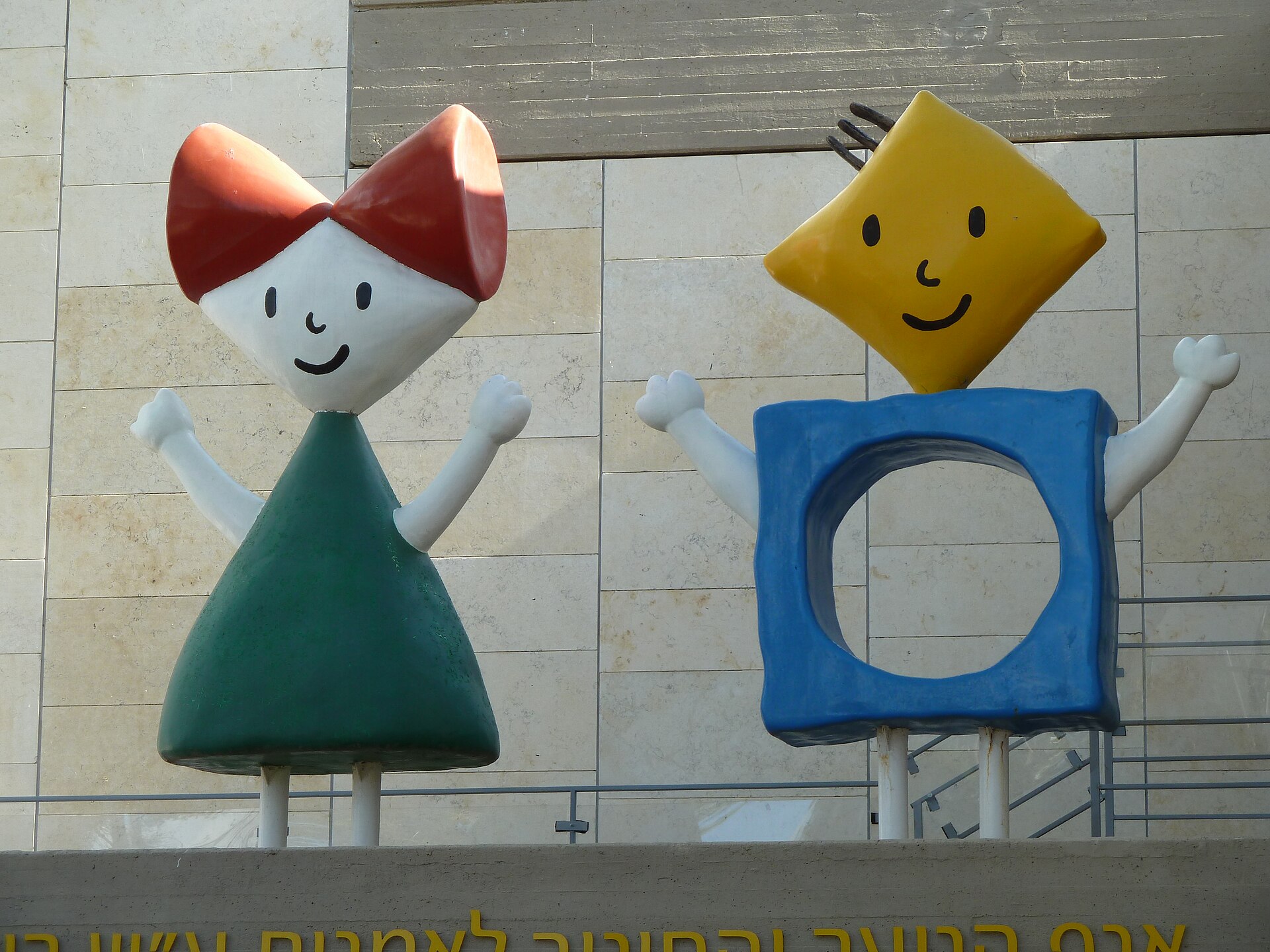 Two colourful waving figures, a girl in a green triangle dress and a boy with a yellow diamond head, above the entrance to the Israel Museum's Ruth Youth Wing