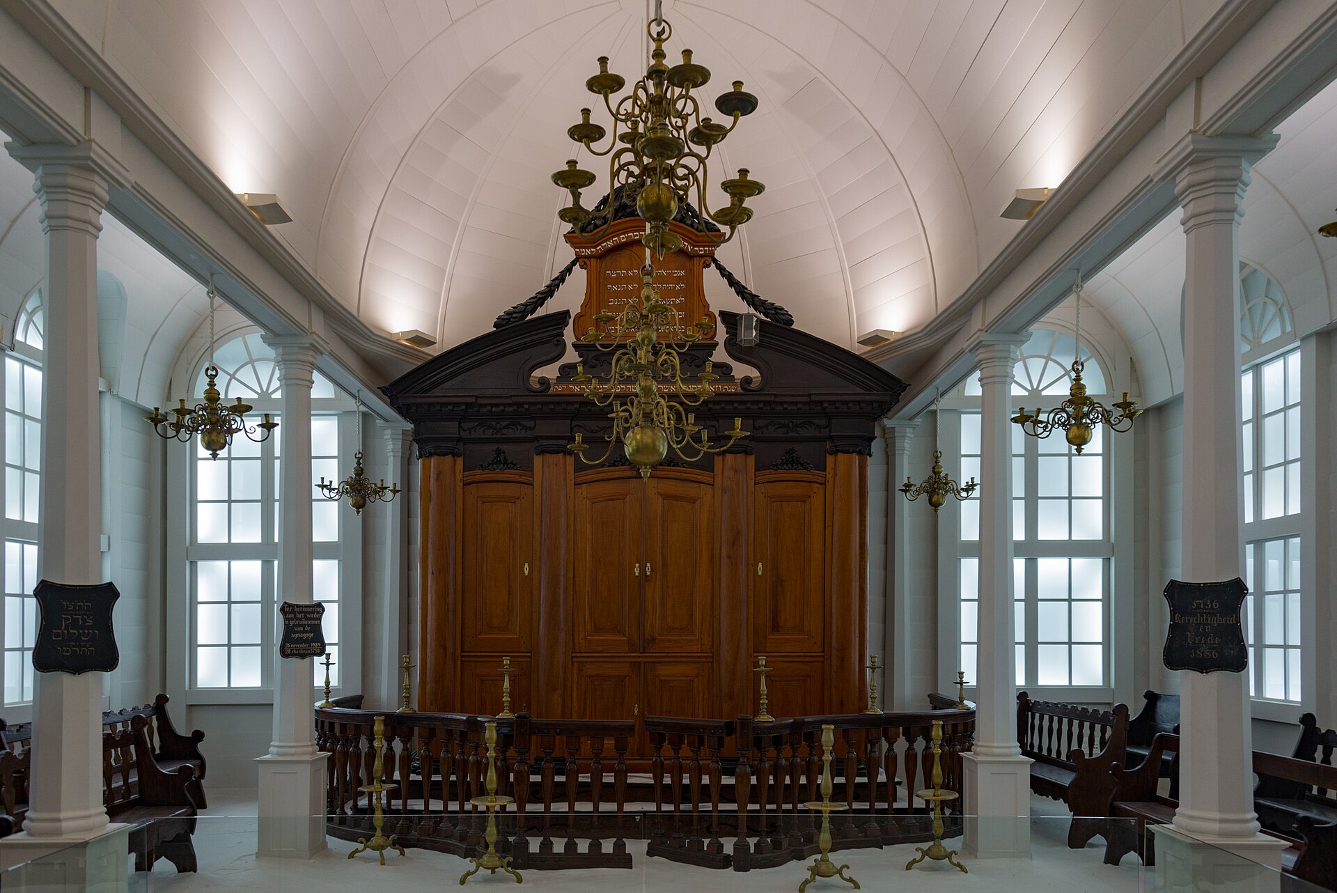The interior of the Tzedek ve-Shalom synagogue from Suriname at the Israel Museum, with a carved wooden Torah ark, brass chandeliers and white columns